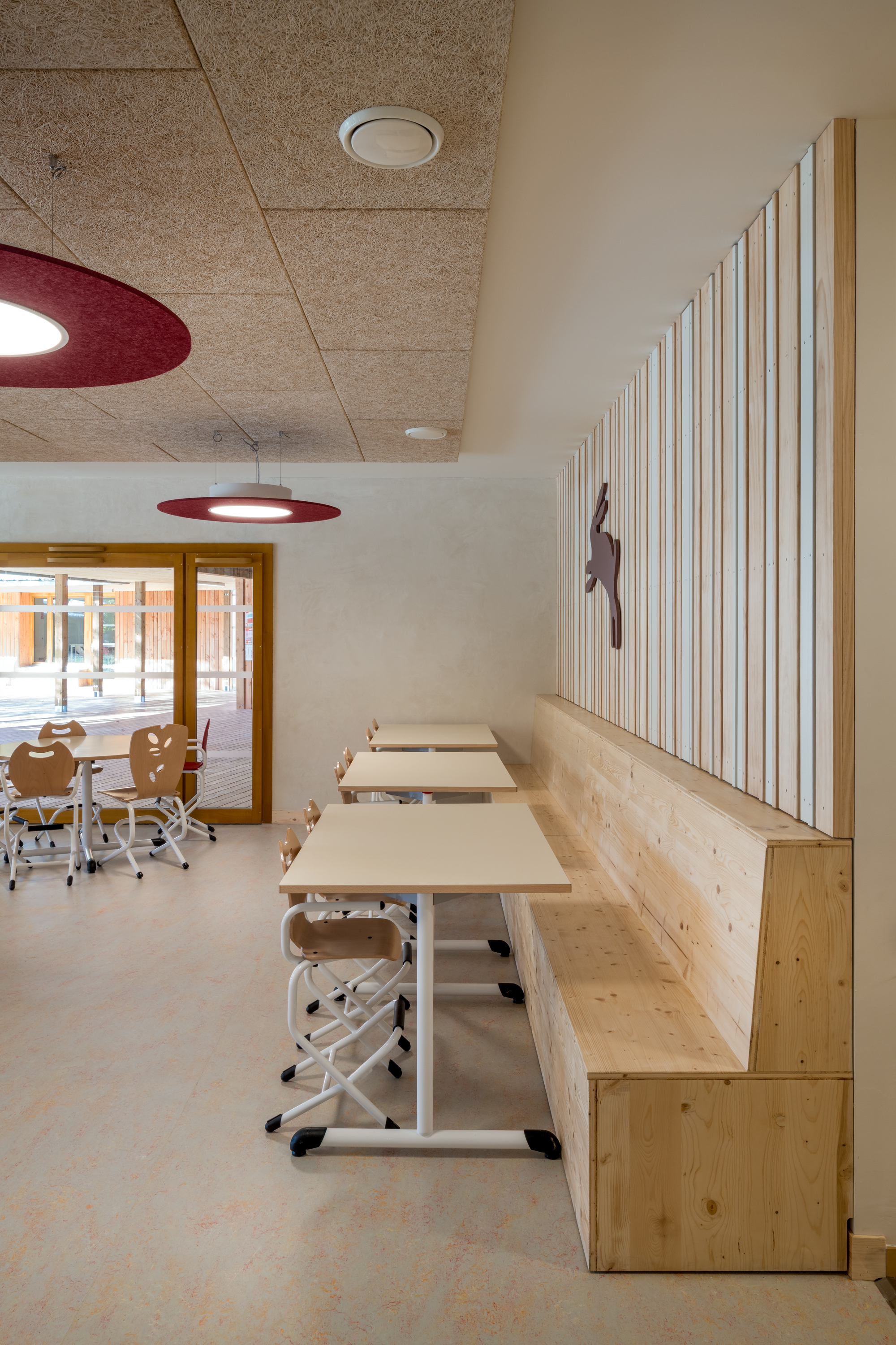 Classroom with maroon disc pendant lights above built-in timber benches and vertical slat wall panel