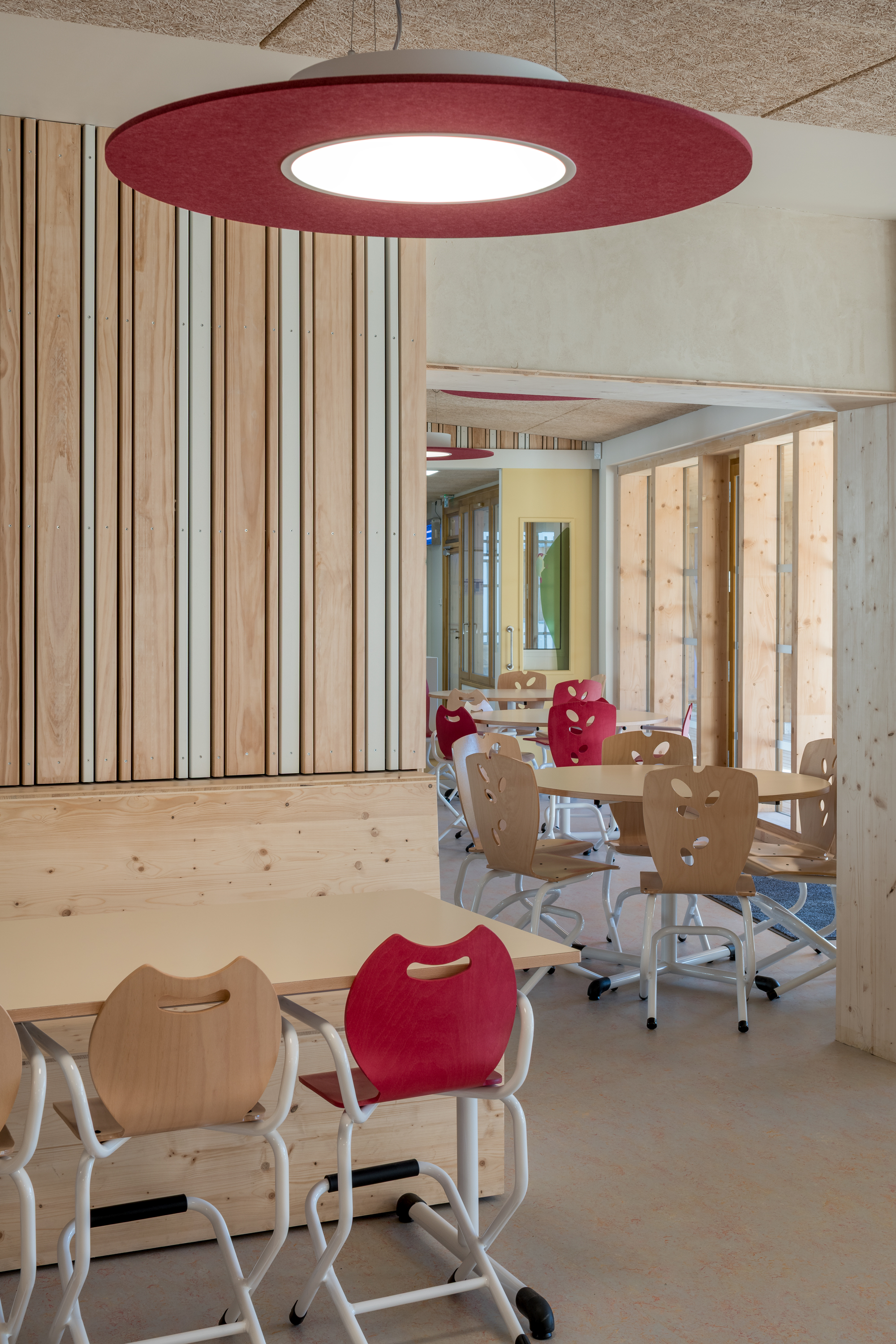 Dining area with maroon disc pendant light and plywood chairs arranged at low tables