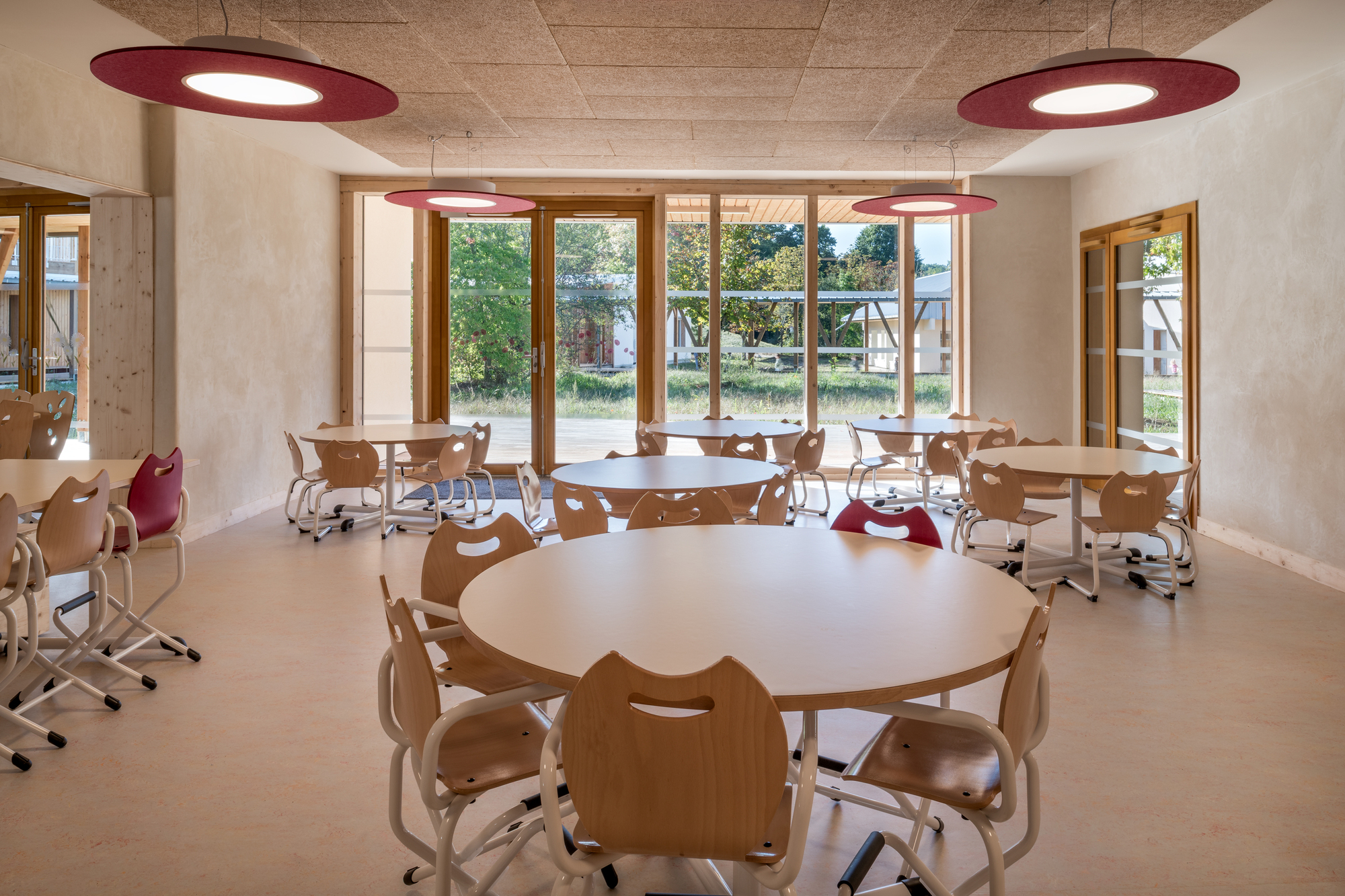 Classroom interior with round timber tables and large windows overlooking the courtyard garden in daylight