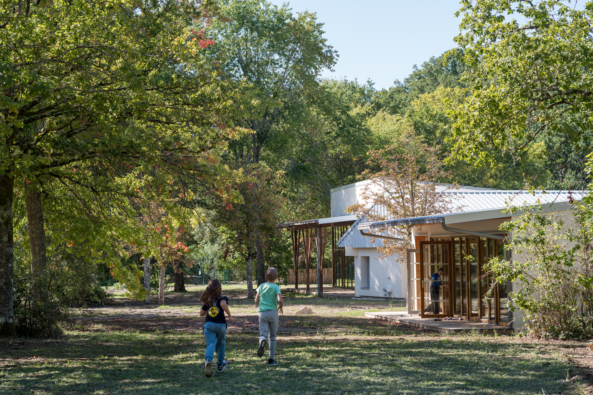 White gabled pavilion with timber columns viewed through trees as two children run across the lawn