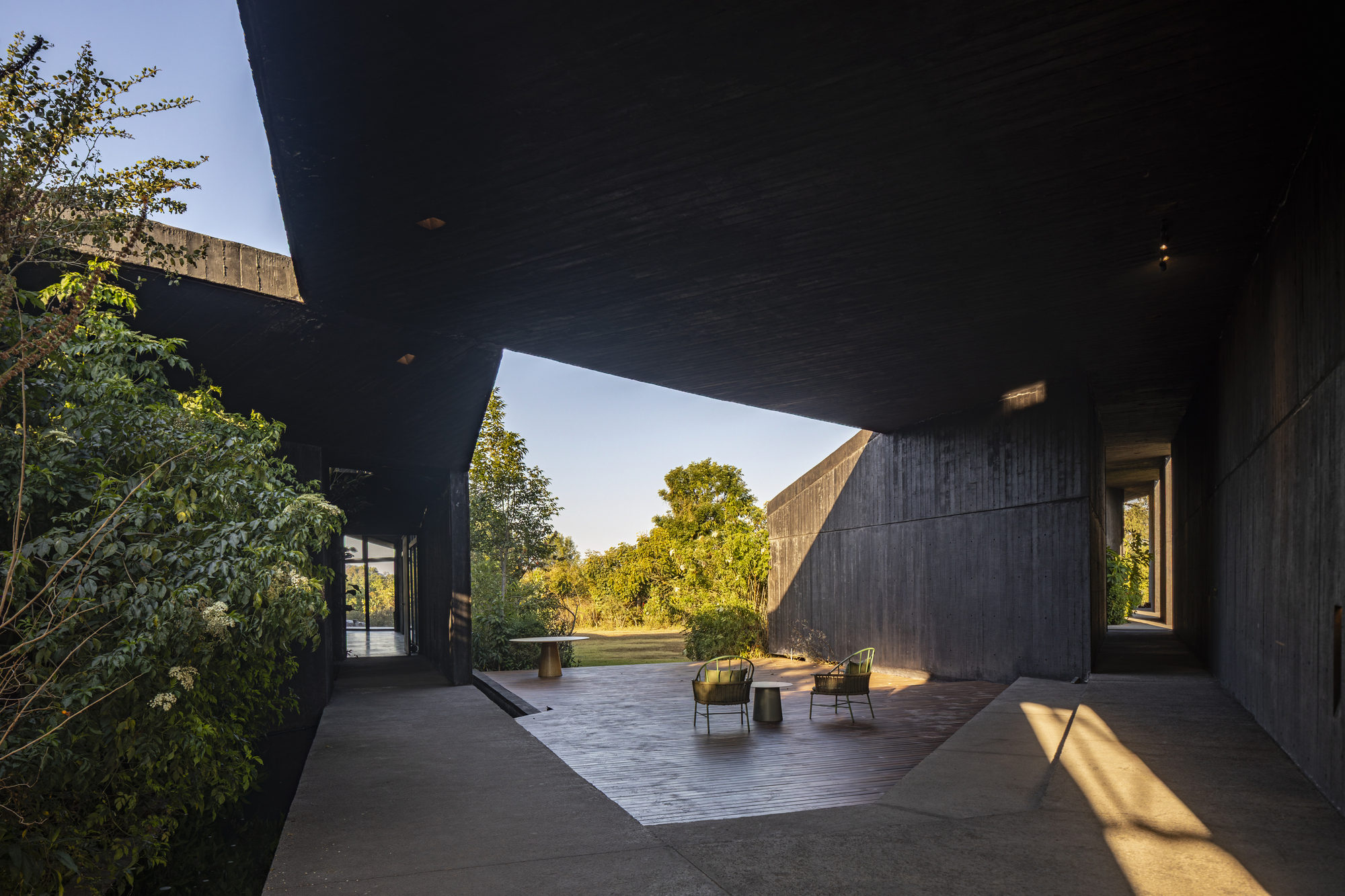 Covered terrace beneath angular concrete planes with scattered seating in late afternoon light