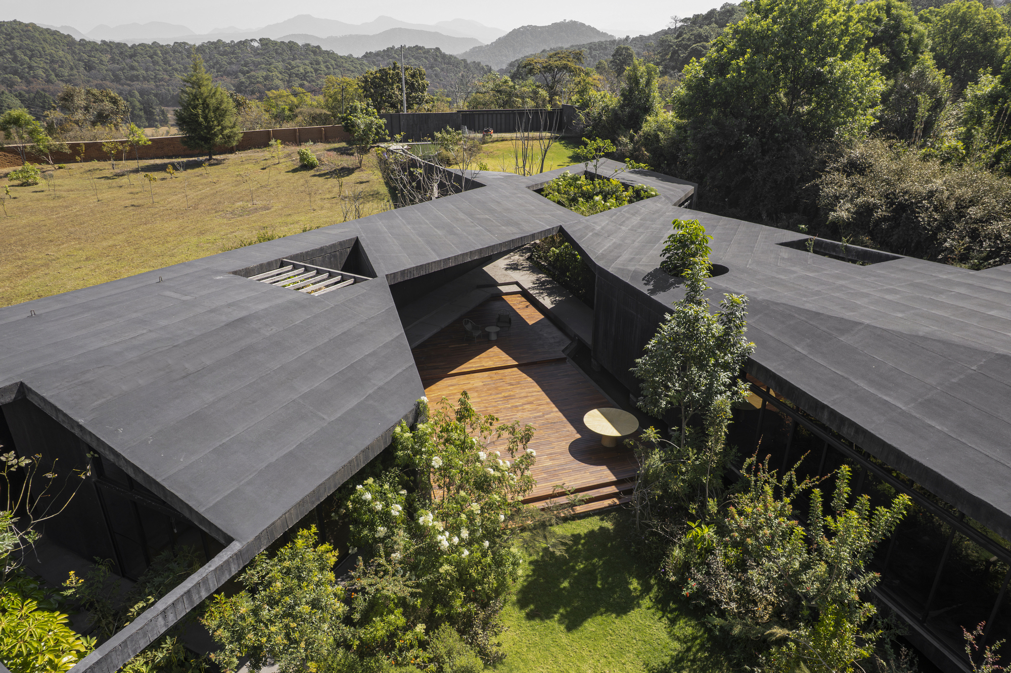Drone view of clustered gabled roofs forming courtyards with planted beds and timber walkways linking the pavilions