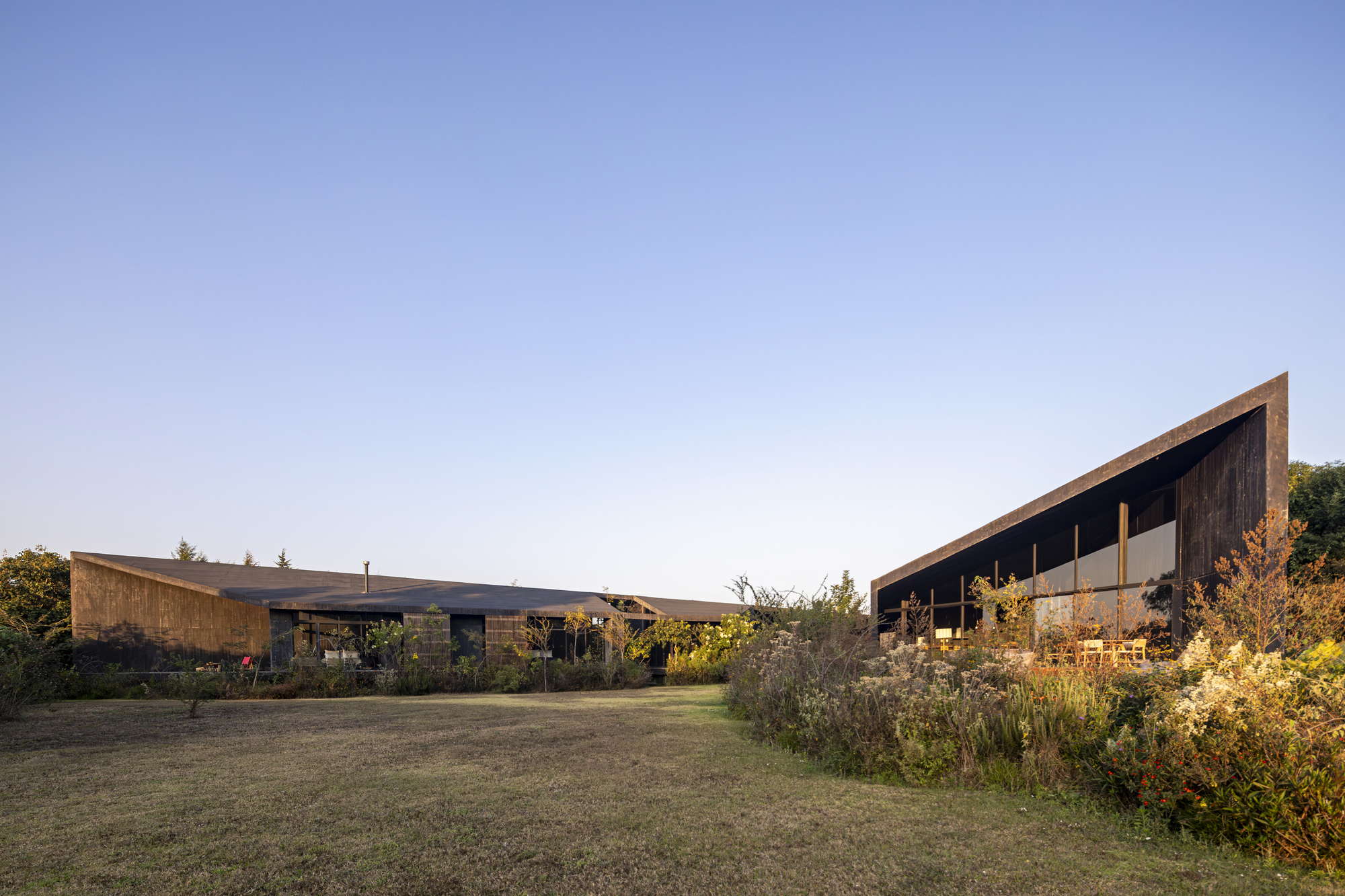 Low-pitched roof pavilions with timber and stone facades separated by open lawn and garden at dusk