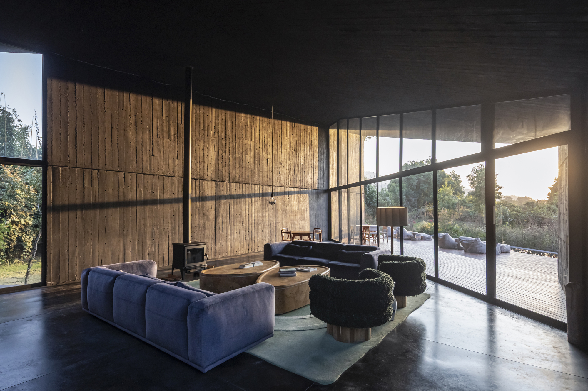 Interior living space with vertical timber wall panels and floor-to-ceiling glazing opening to timber deck at sunset
