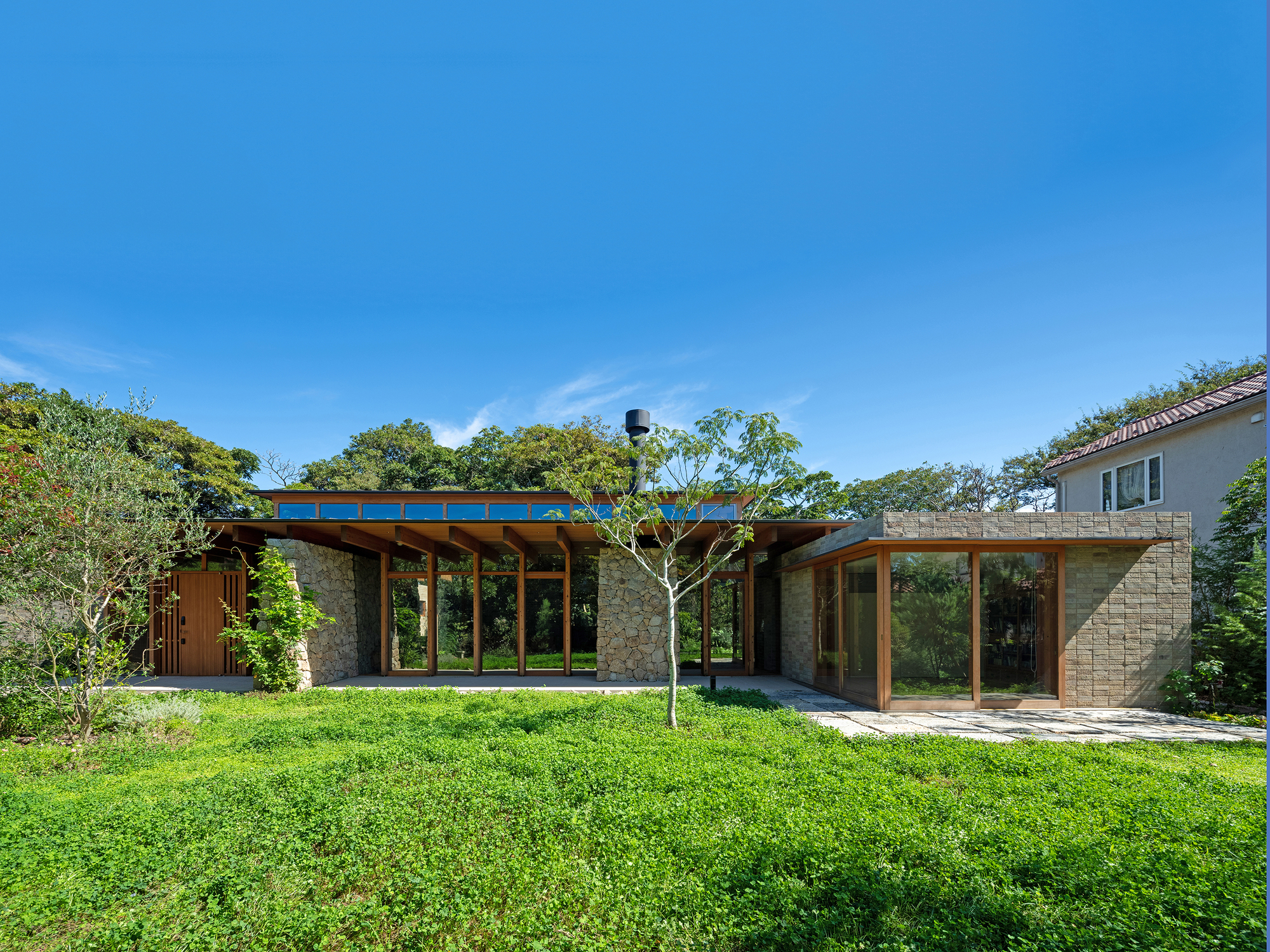 Garden elevation showing stone walls and timber-framed glazing under a flat roof on a sunny day