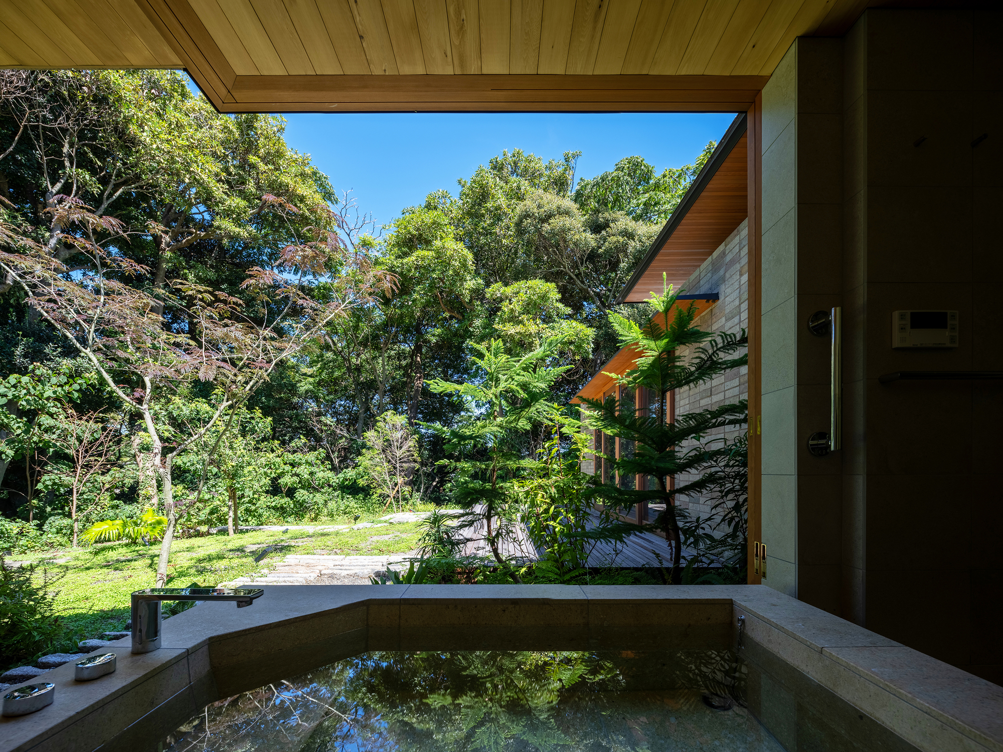 Concrete soaking tub on covered terrace opening to lawn and forest in bright daylight