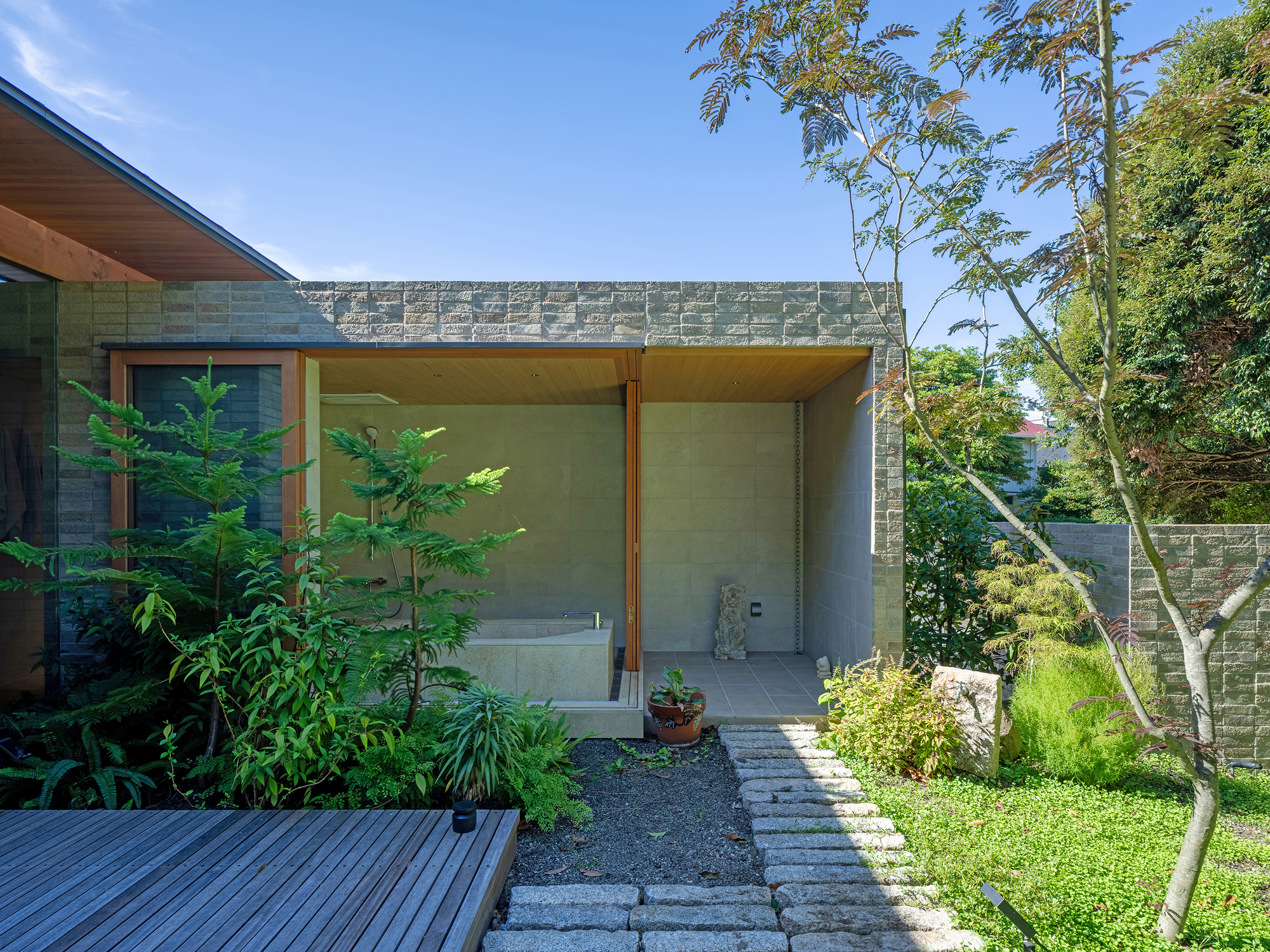 Covered outdoor bathing area with concrete block wall and timber ceiling overlooking garden with stepping stones