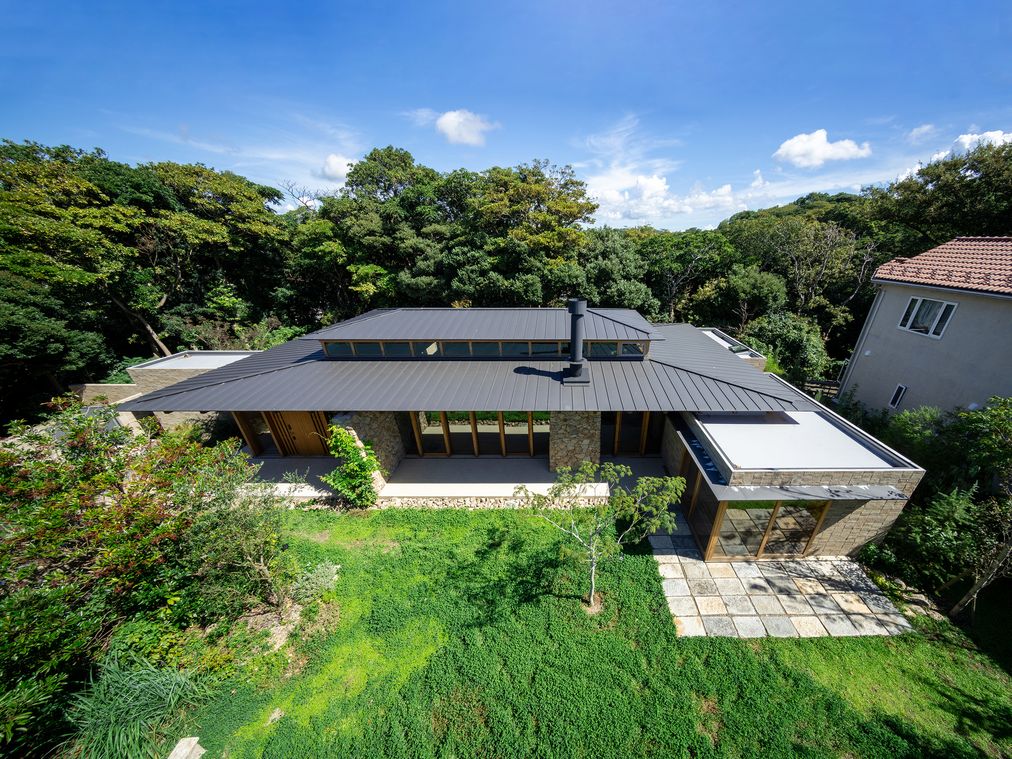 Aerial view of the low-slung metal roof volumes surrounded by lawn and forest canopy