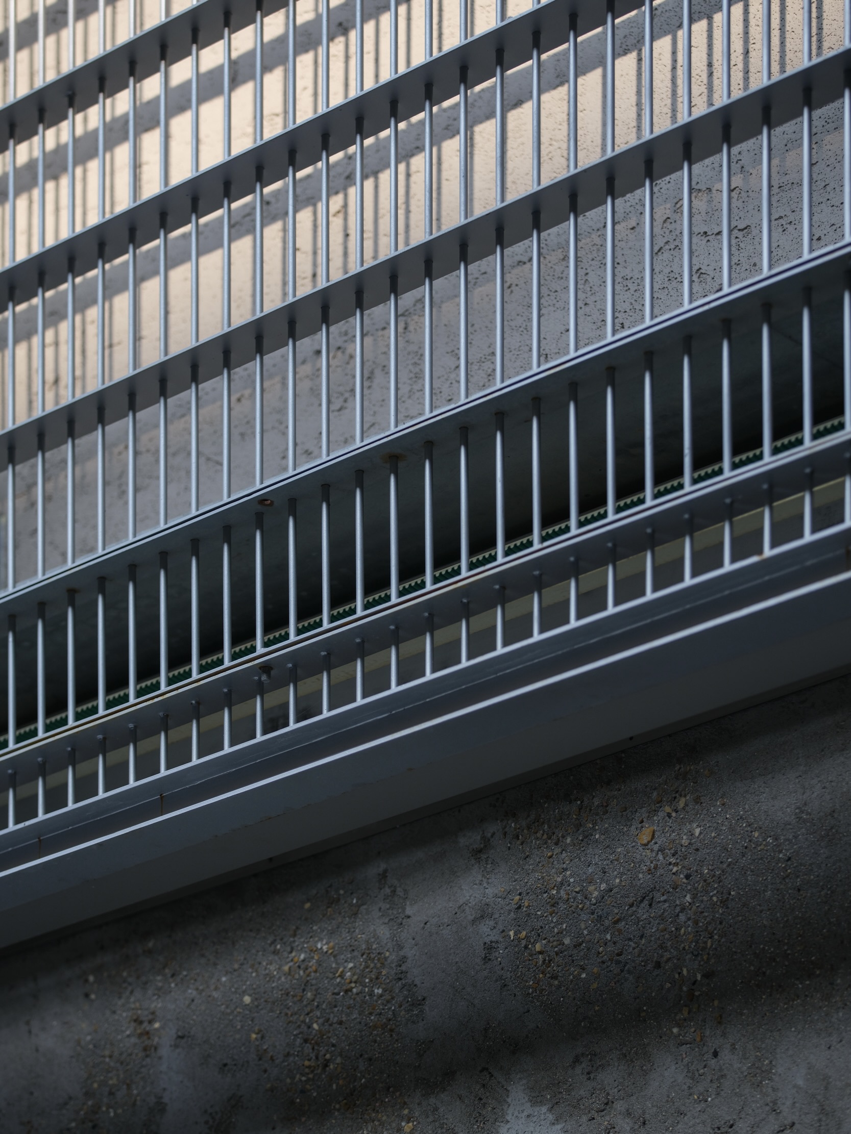Detail of metal balustrade with vertical fins and horizontal rails meeting a concrete floor