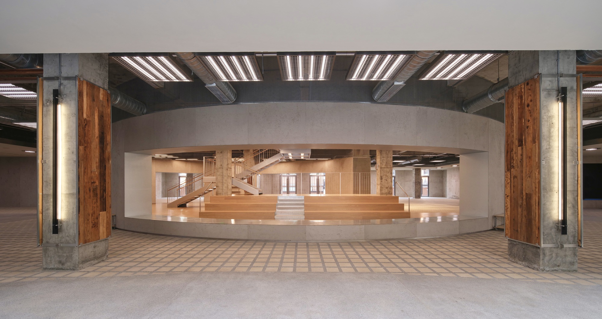 View through a curved opening into a timber-lined atrium with staircases and balconies under exposed beams