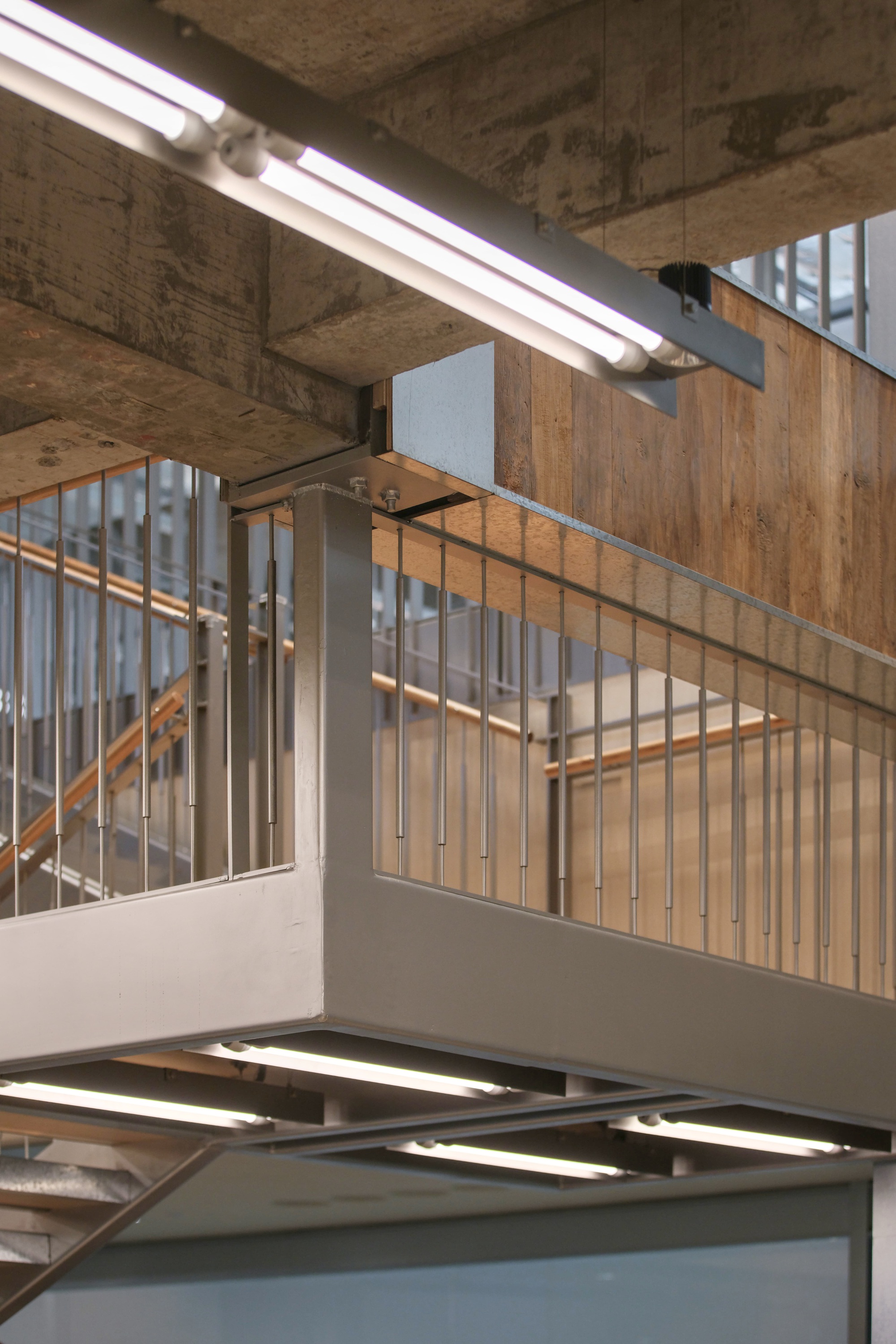 Stairwell with timber slat balustrades and exposed concrete ceiling beams with fluorescent tube lighting