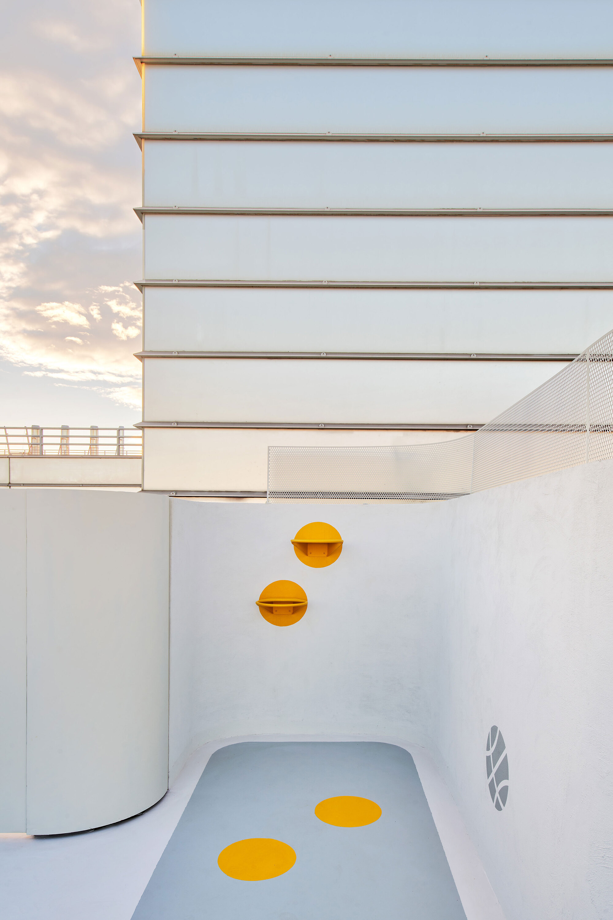 White play slide with yellow circular accents beside horizontal metal cladding at dusk