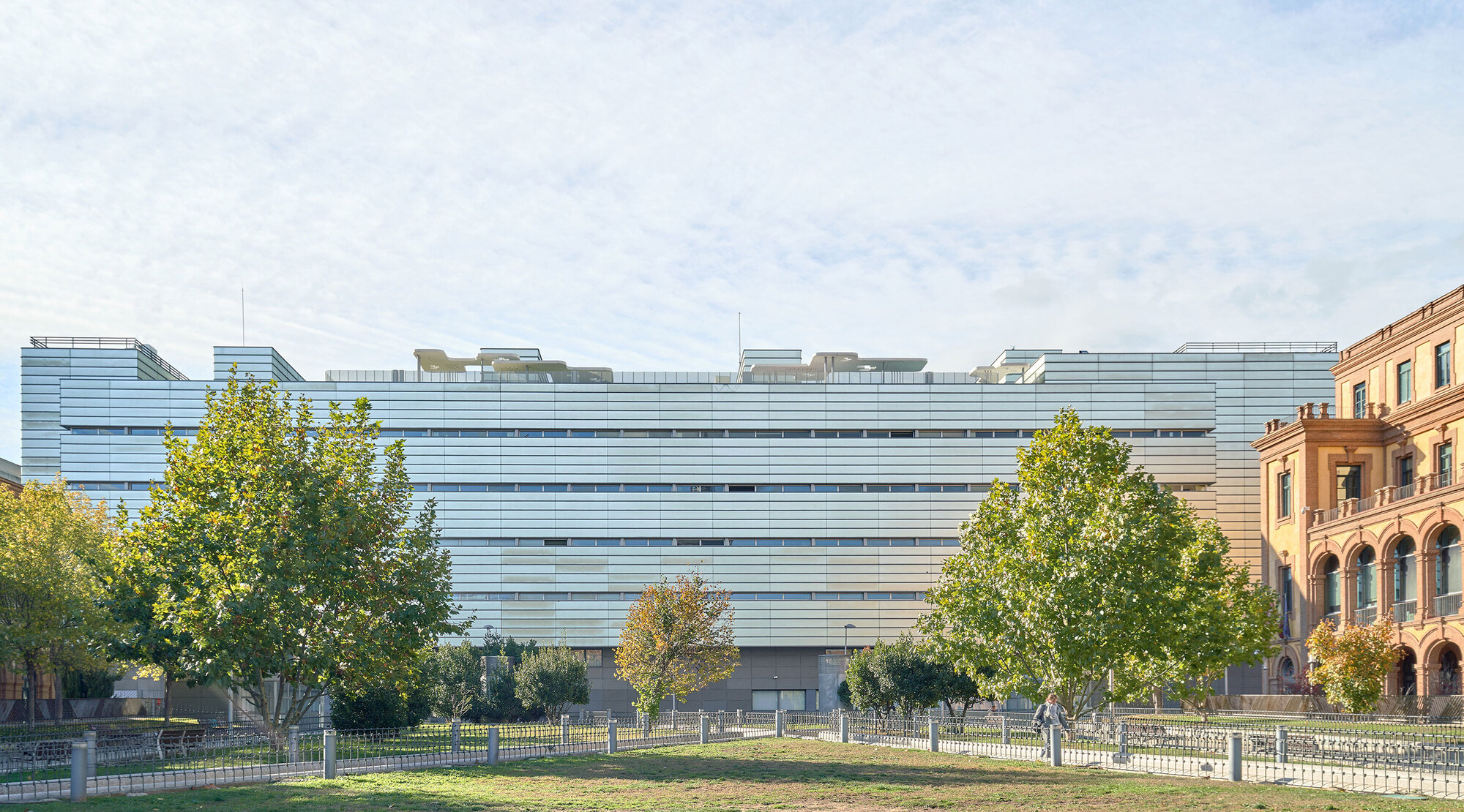 Horizontal louvered facade spanning multiple stories with trees in the foreground and a lawn below