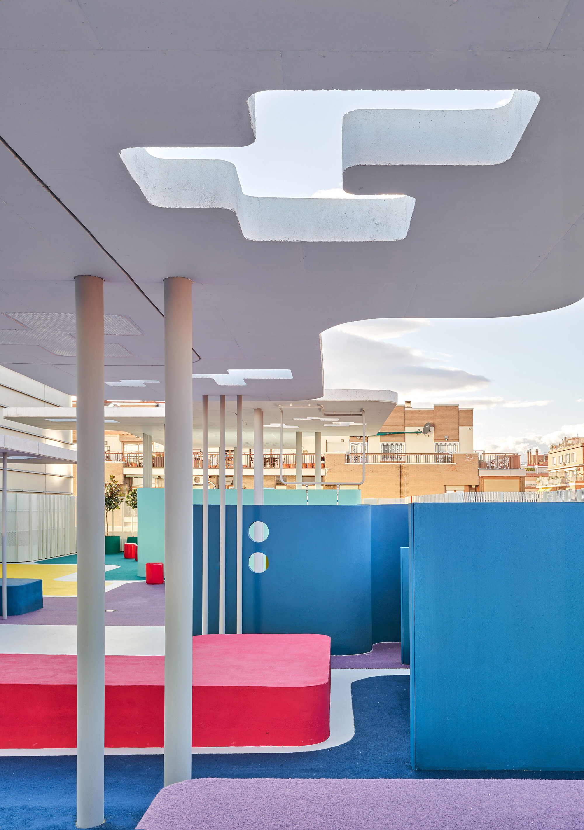 Interior rooftop space with curved colorful seating platforms, white columns, and sculptural ceiling cutouts