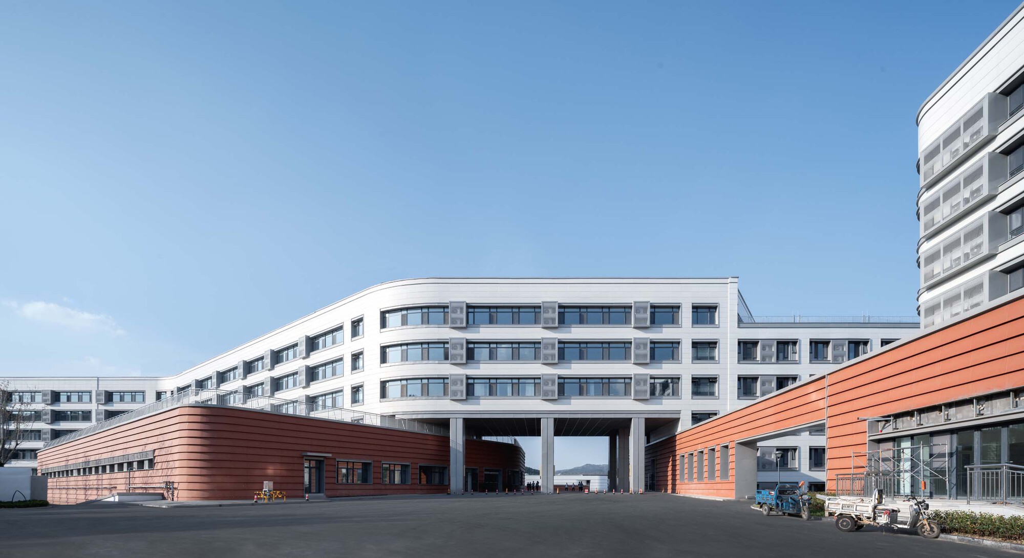 White concrete block elevated on columns over two red-clad horizontal volumes under clear blue sky