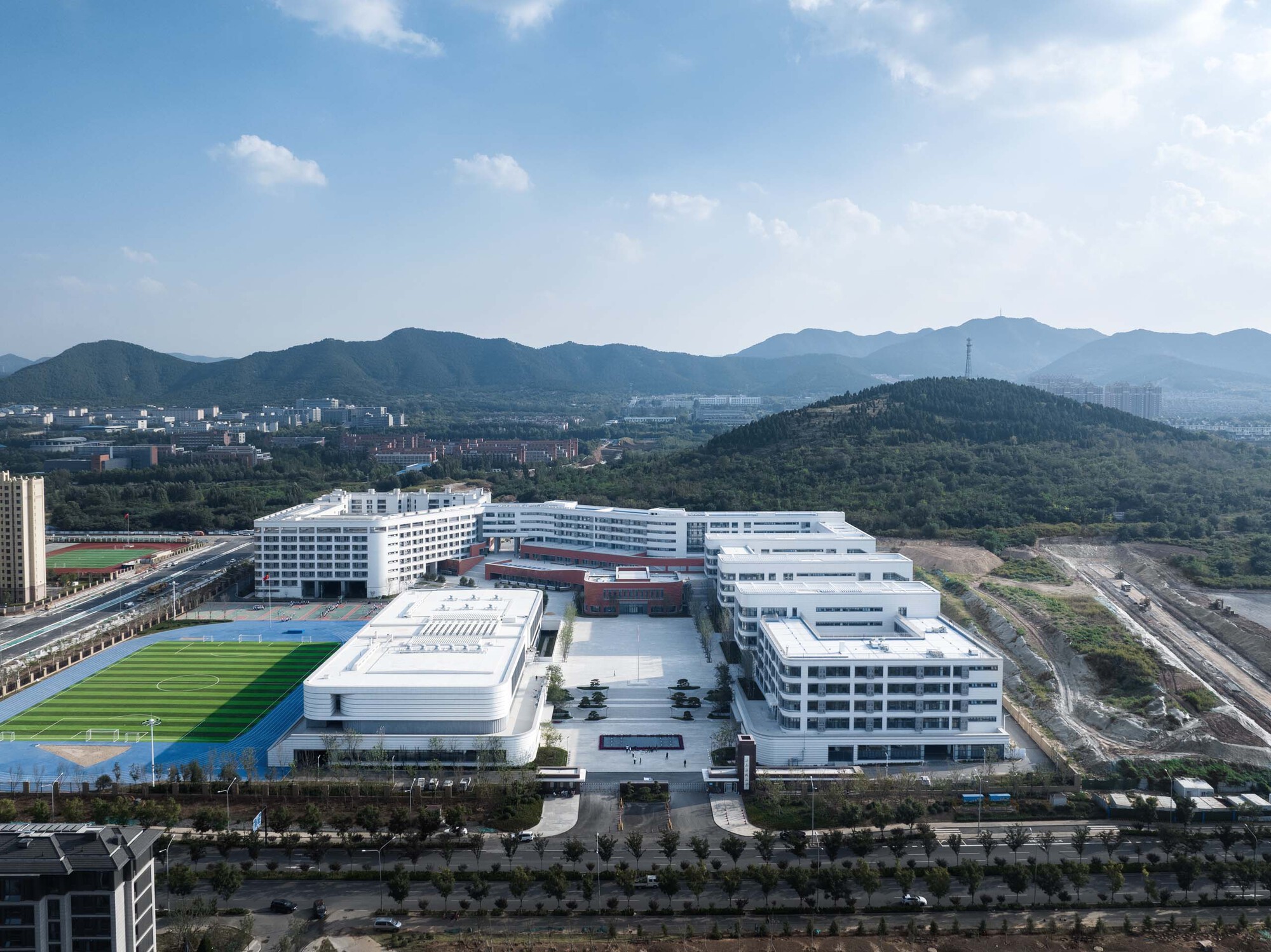 Aerial view of the white campus with athletic fields and terraced courtyards backed by forested hills