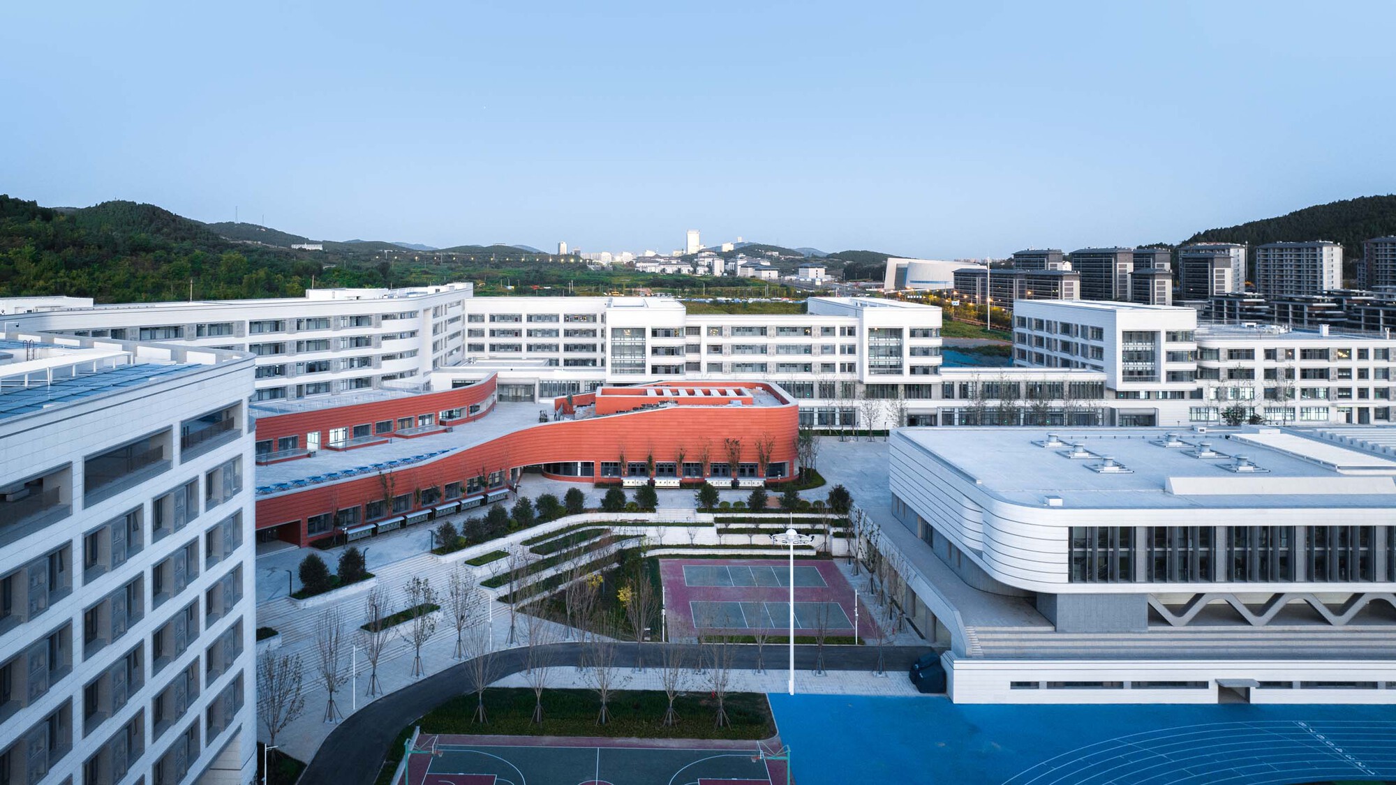 Central courtyard with tennis courts and planted terraces framed by white buildings and red volumes
