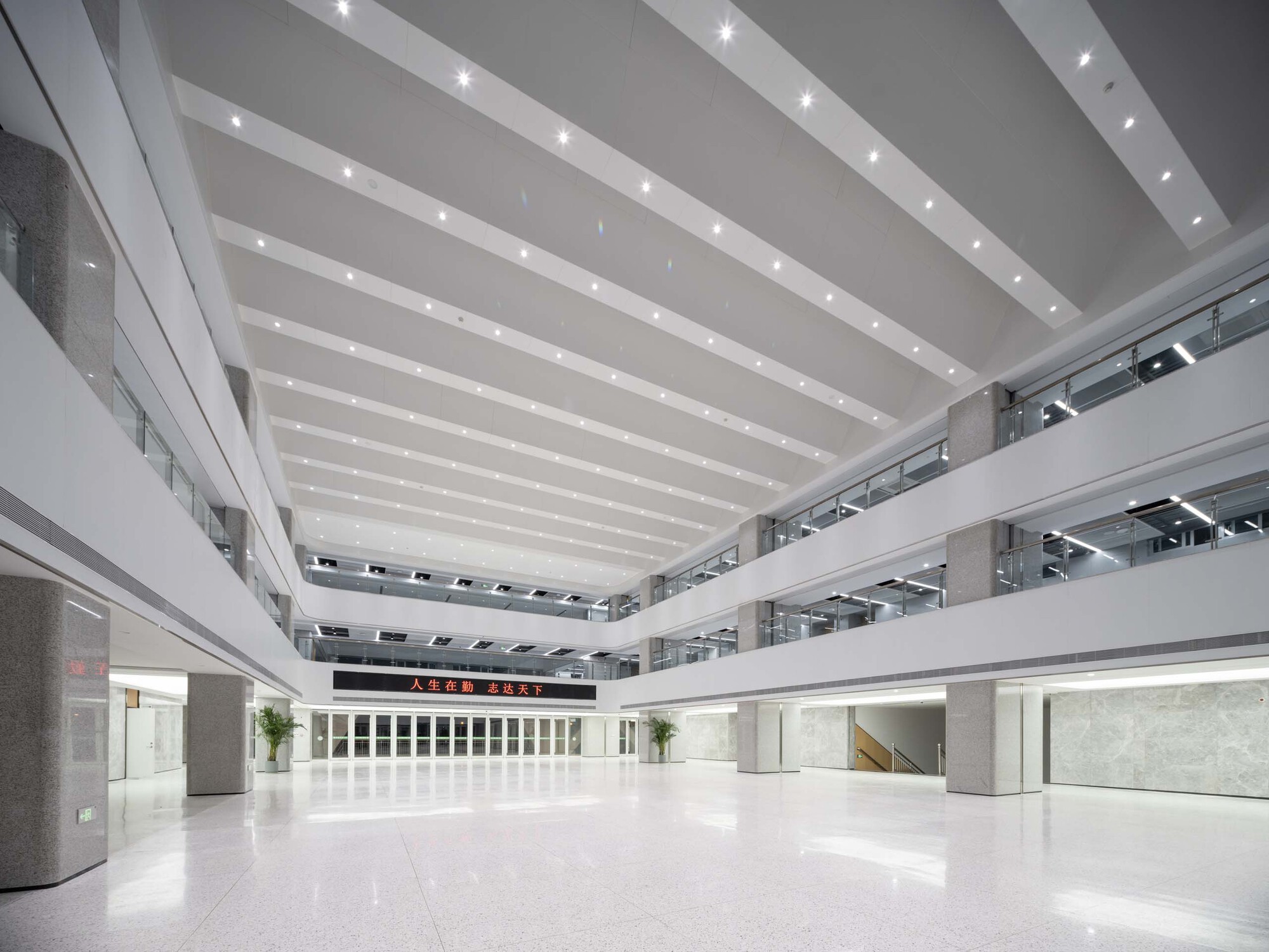 Multi-story interior atrium with white terrazzo floors and horizontal ceiling bands with integrated lighting