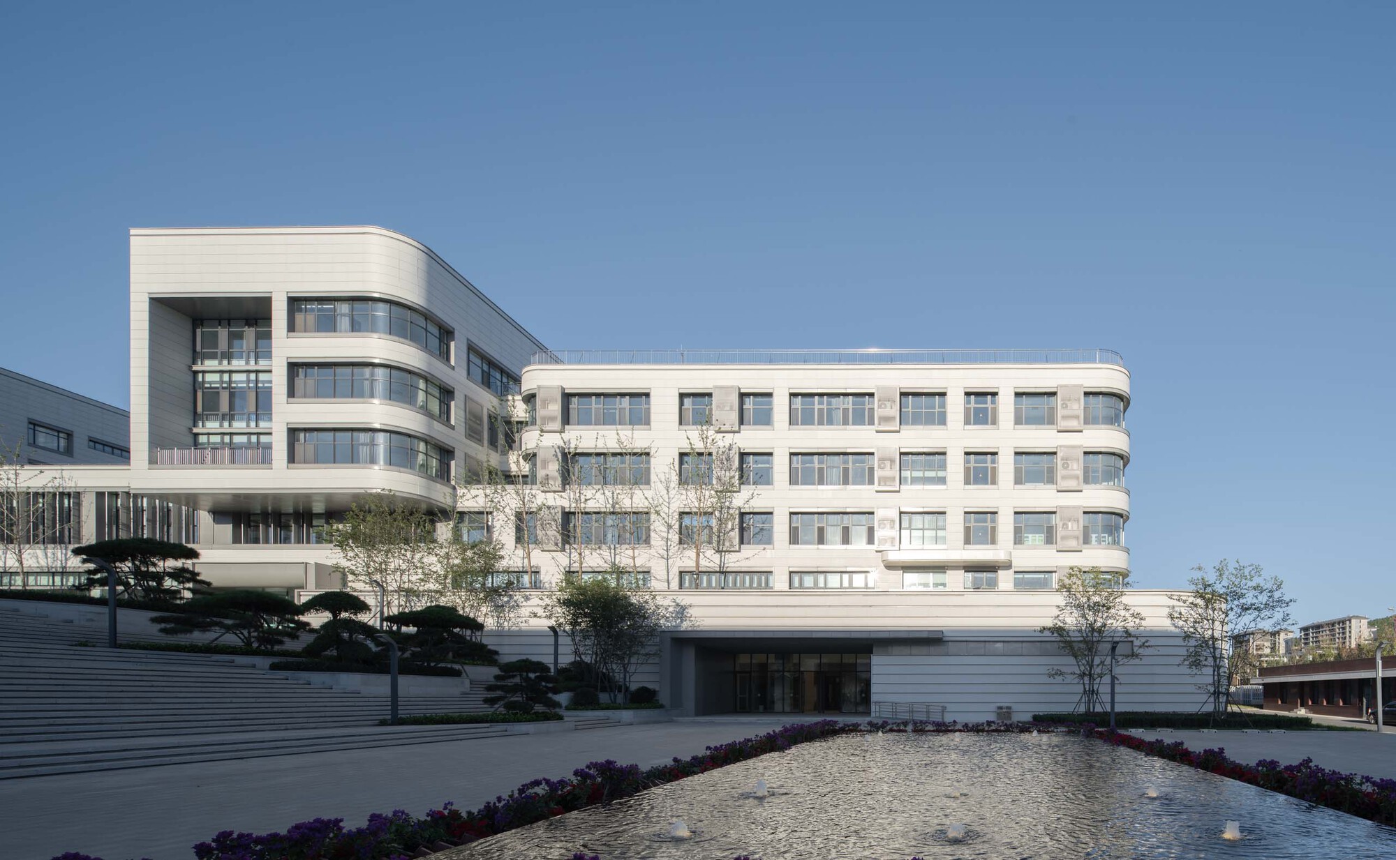 Curved white facade with horizontal window bands rising above reflecting pool edged with planted beds