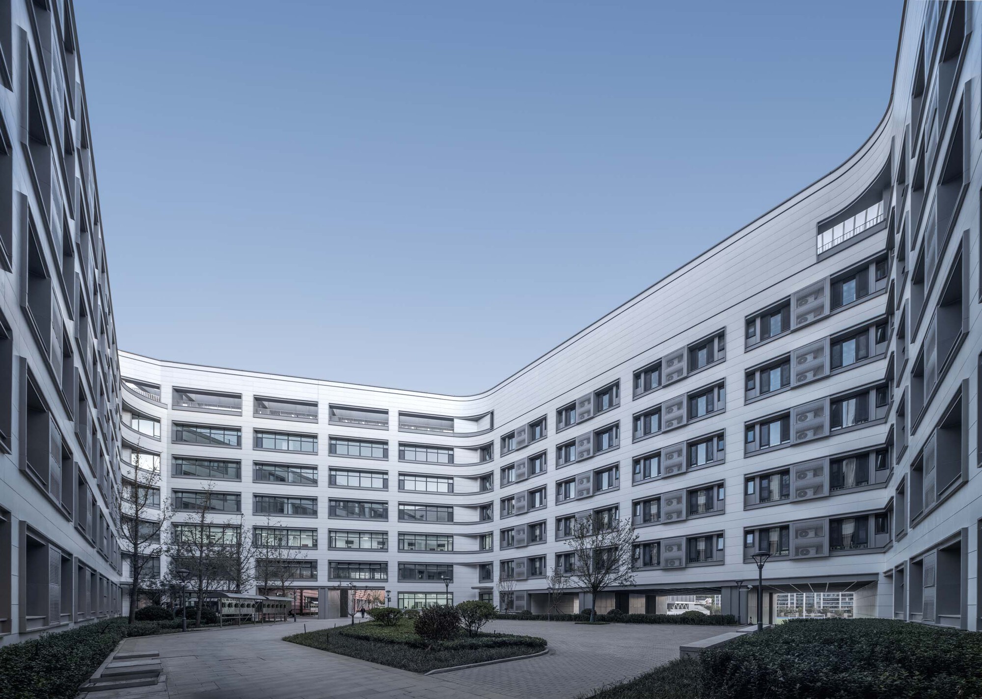 Interior courtyard enclosed by curved white facades with planted beds and bare trees under grey sky