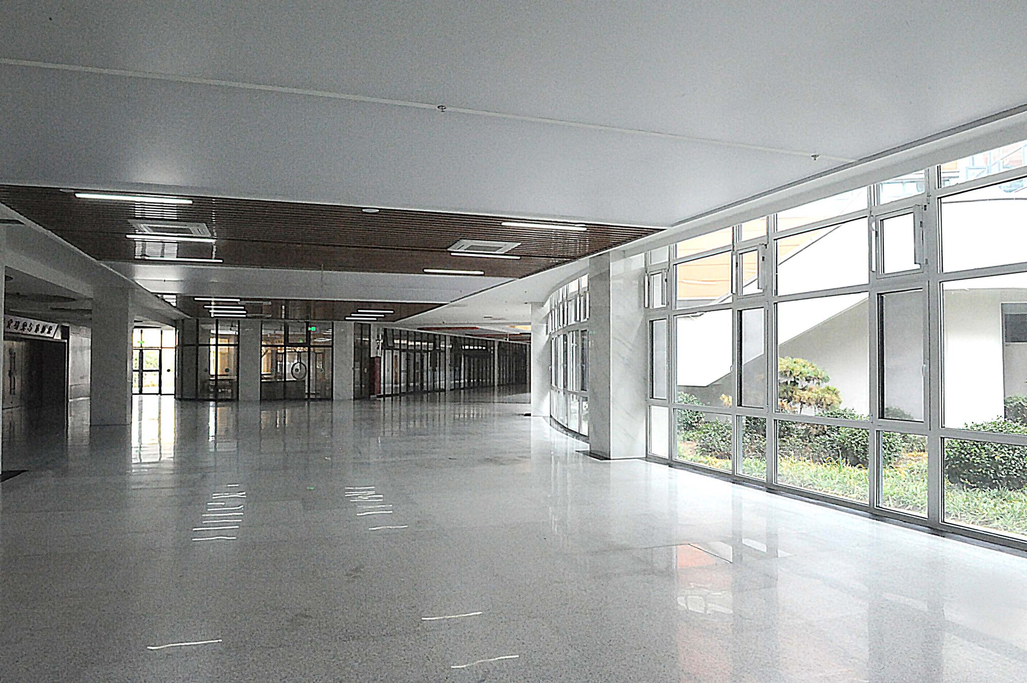 Interior corridor with polished terrazzo flooring and floor-to-ceiling windows overlooking greenery