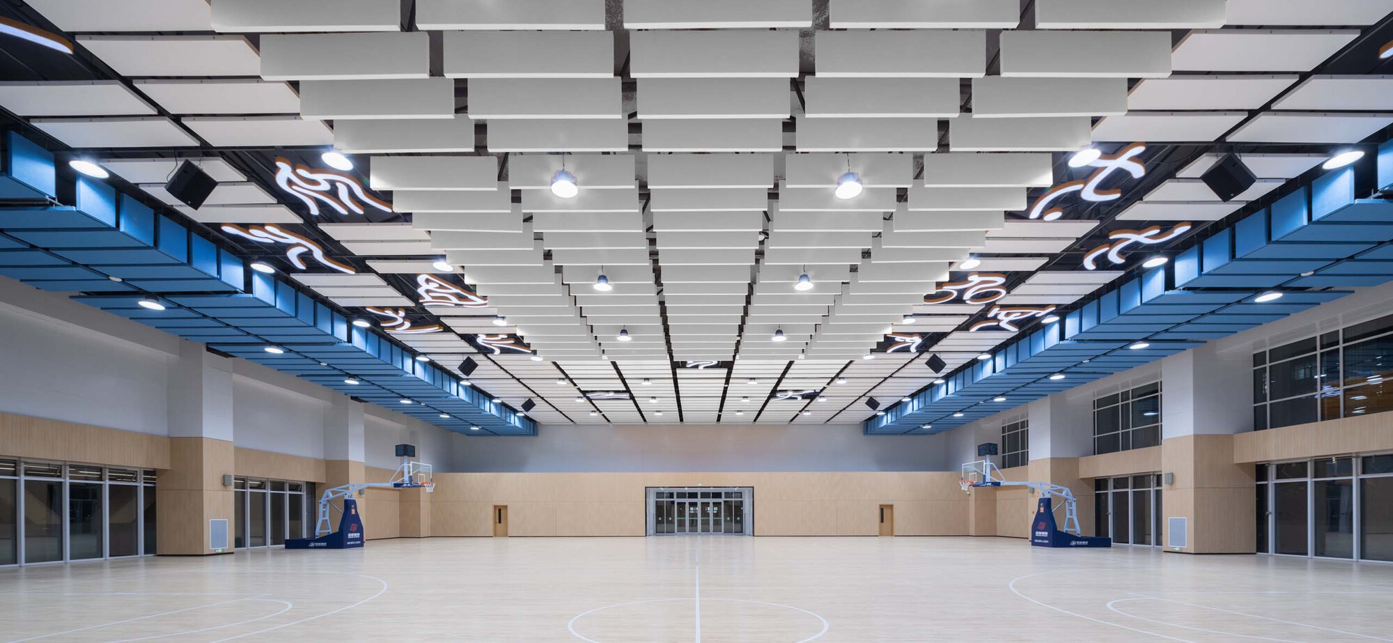 Indoor basketball court with suspended acoustic ceiling panels and high clerestory windows