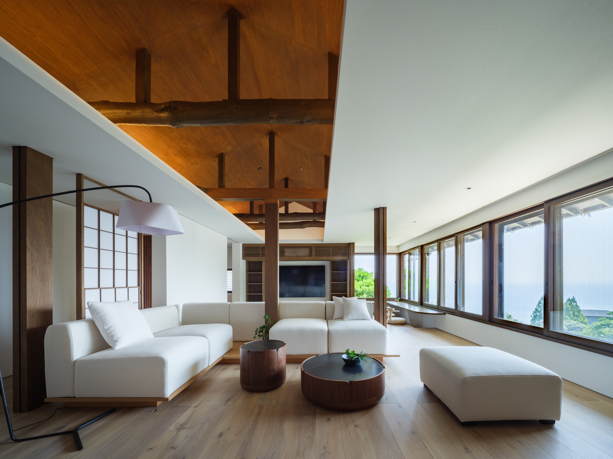 Living room with exposed timber ceiling beams and horizontal window band framing a distant ocean view