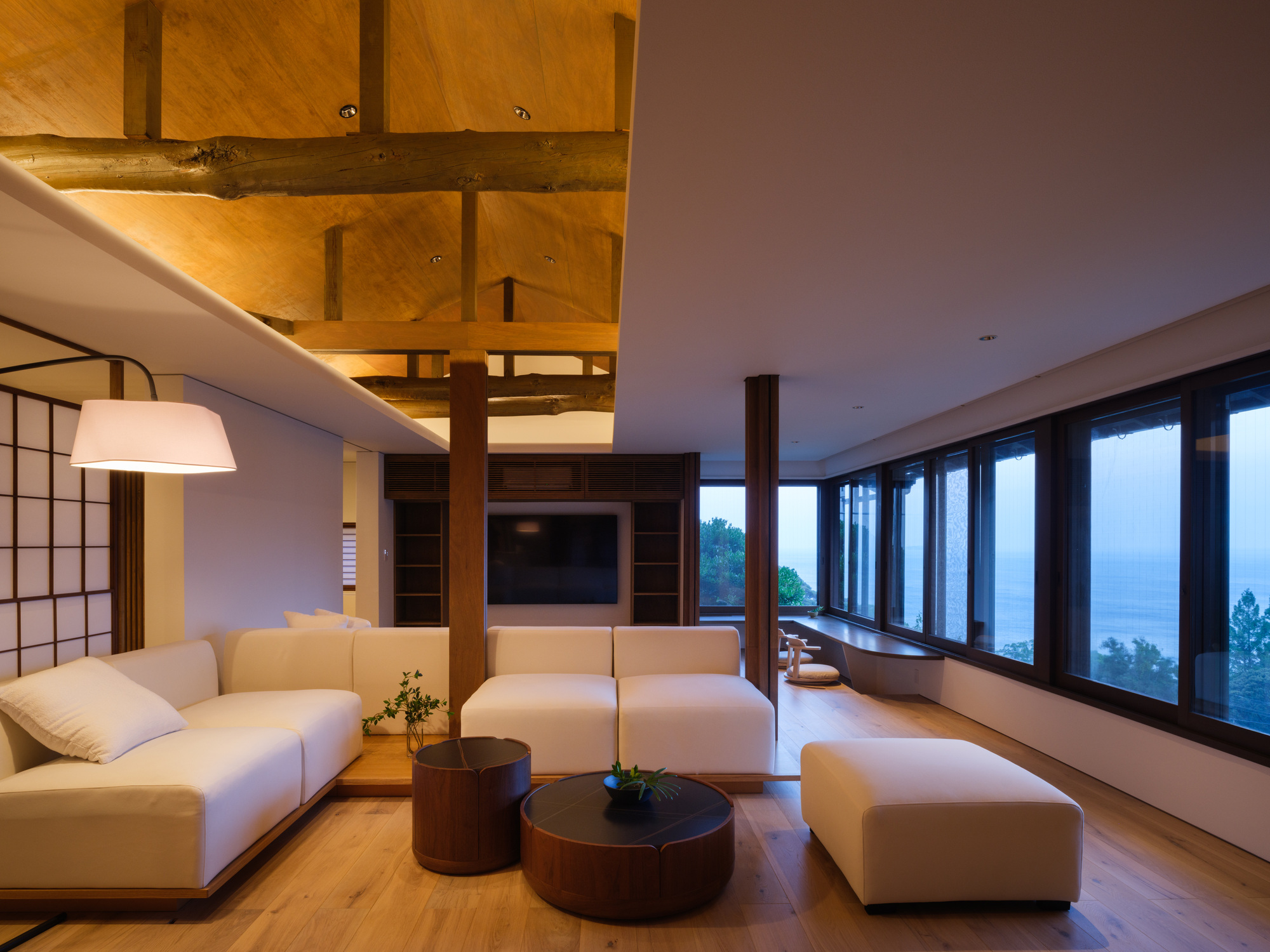 Living room with exposed timber ceiling structure and continuous window wall at dusk