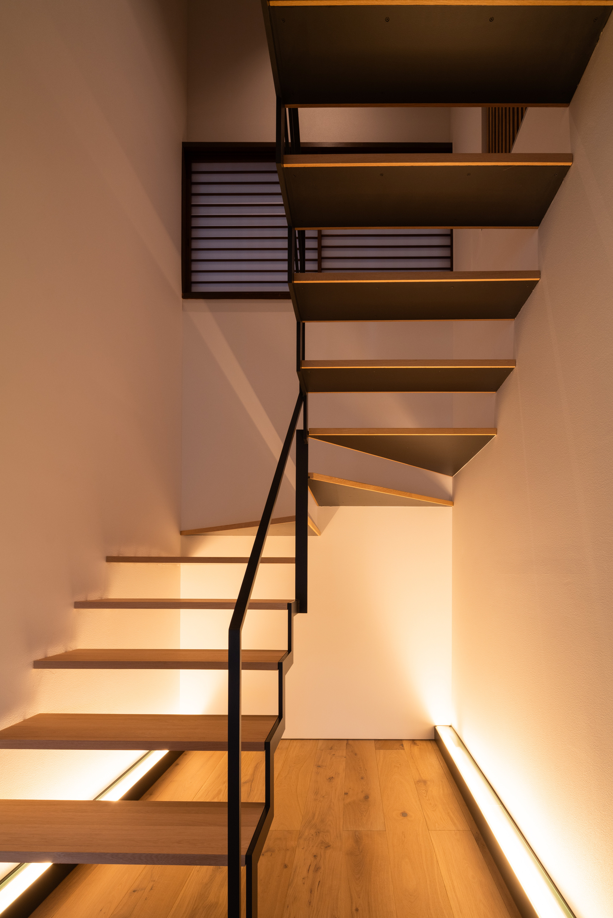 Floating timber staircase with black steel railing and integrated LED strip lighting in white walls
