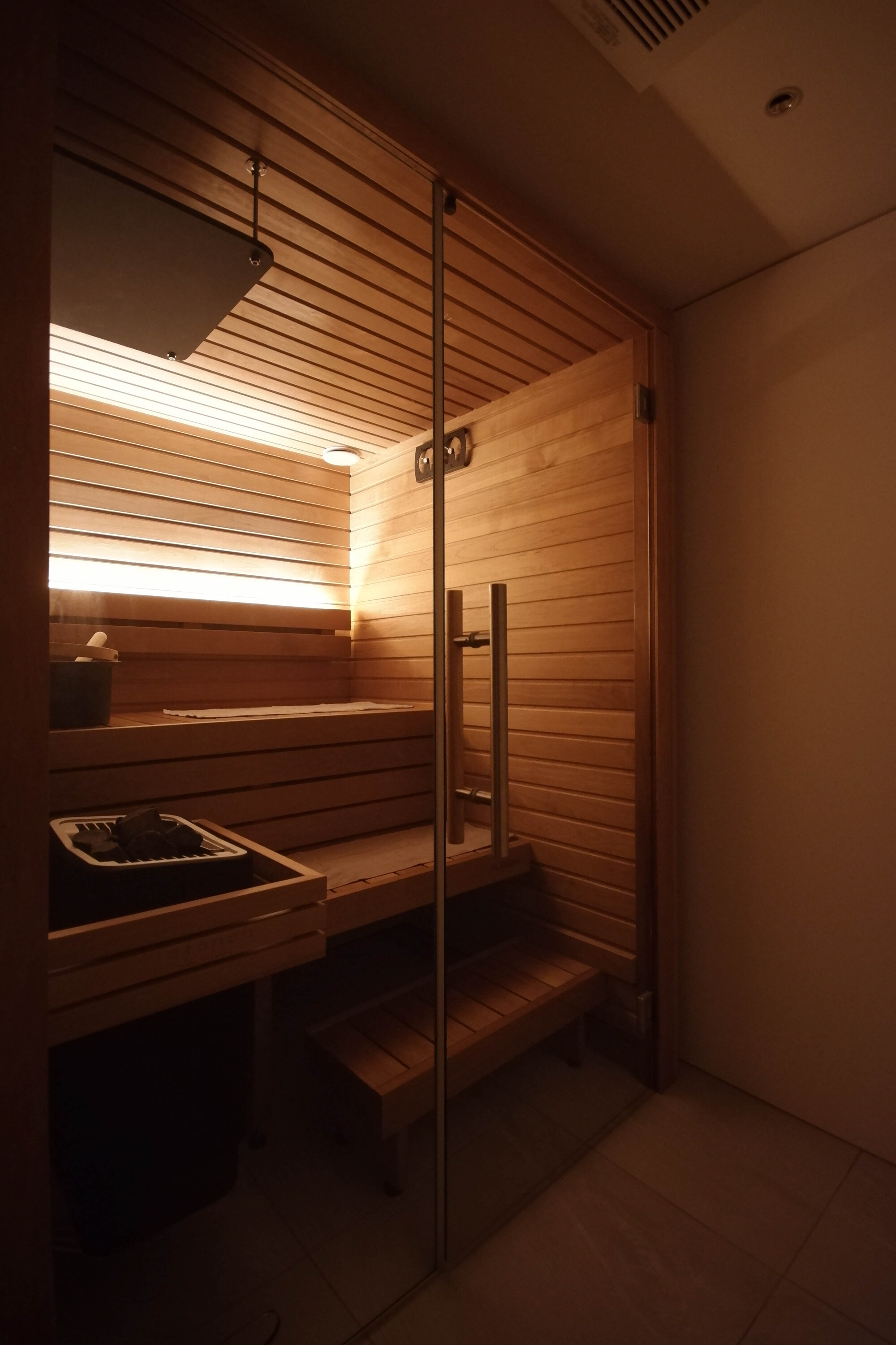 Wood-lined sauna with horizontal slat benches and glass door under warm recessed lighting