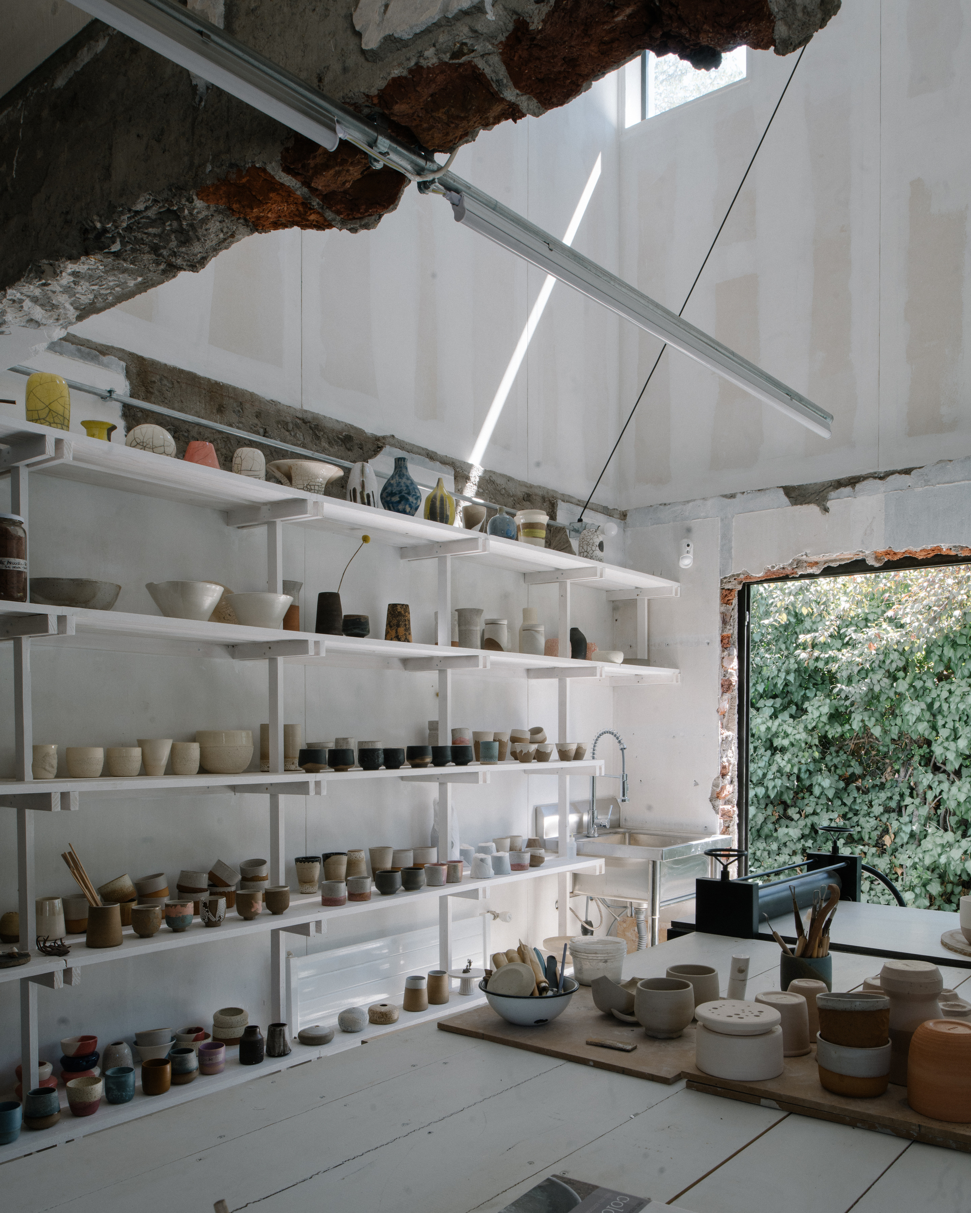 Pottery workshop with white shelving and exposed brick openings under skylit ceiling