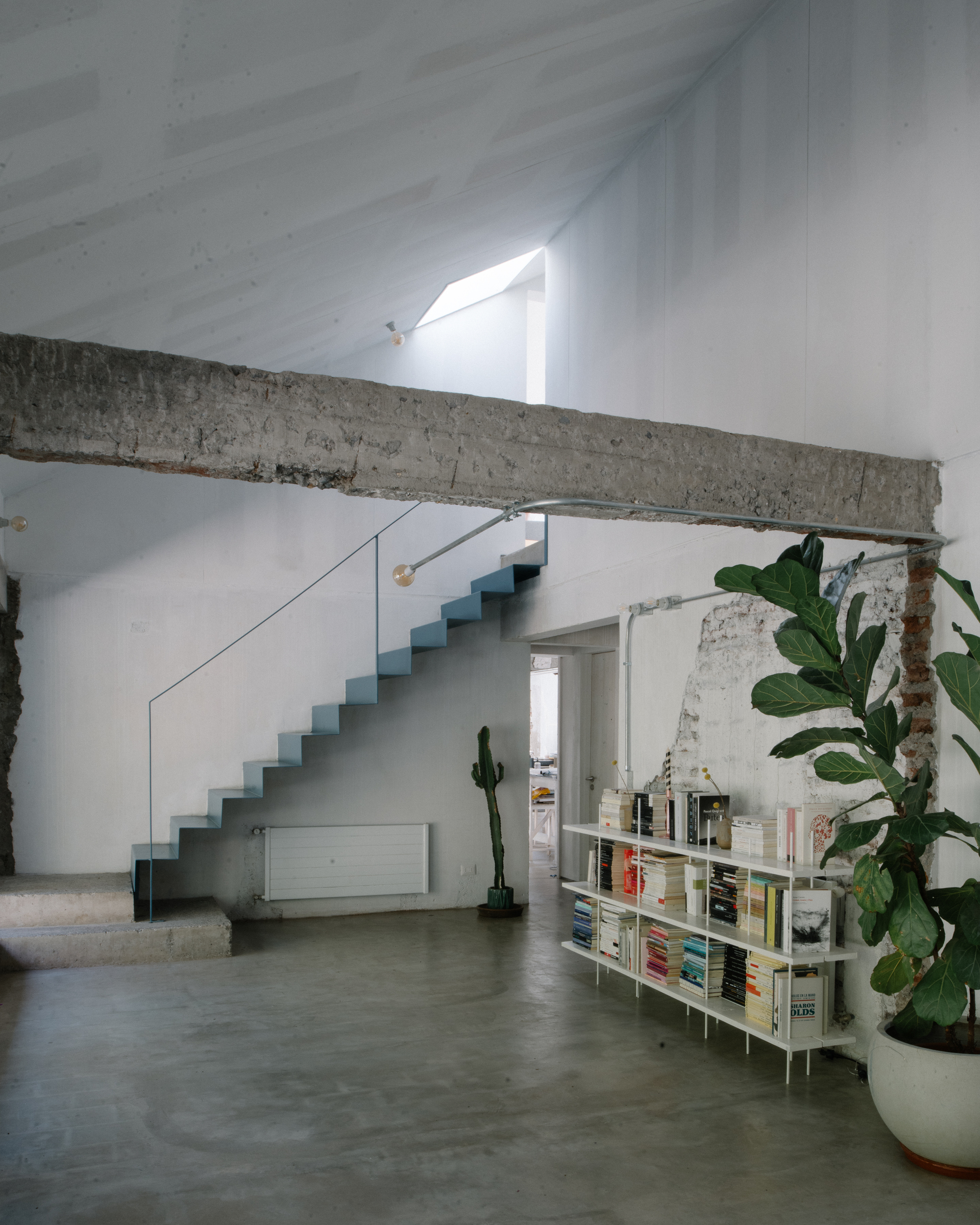 Double-height interior with blue metal staircase, exposed concrete beam, and slanted skylight above