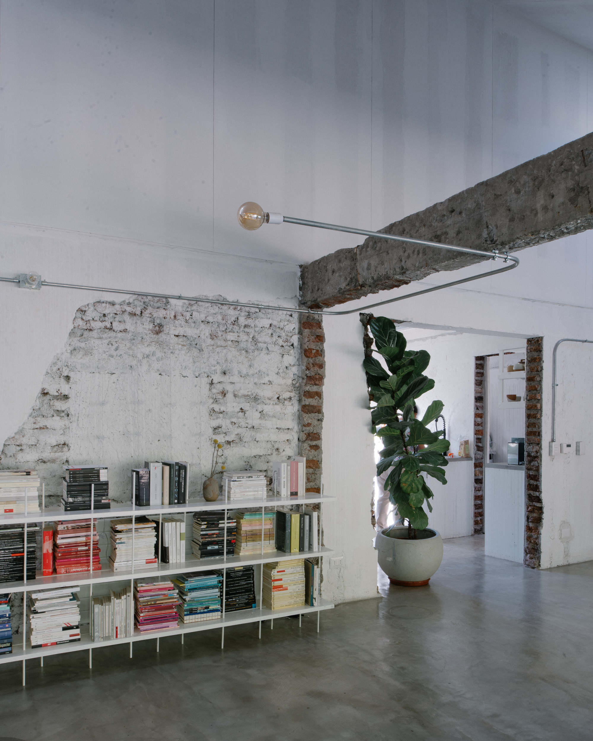 Looking up at exposed concrete beam with pendant light fixture and whitewashed brick partition below