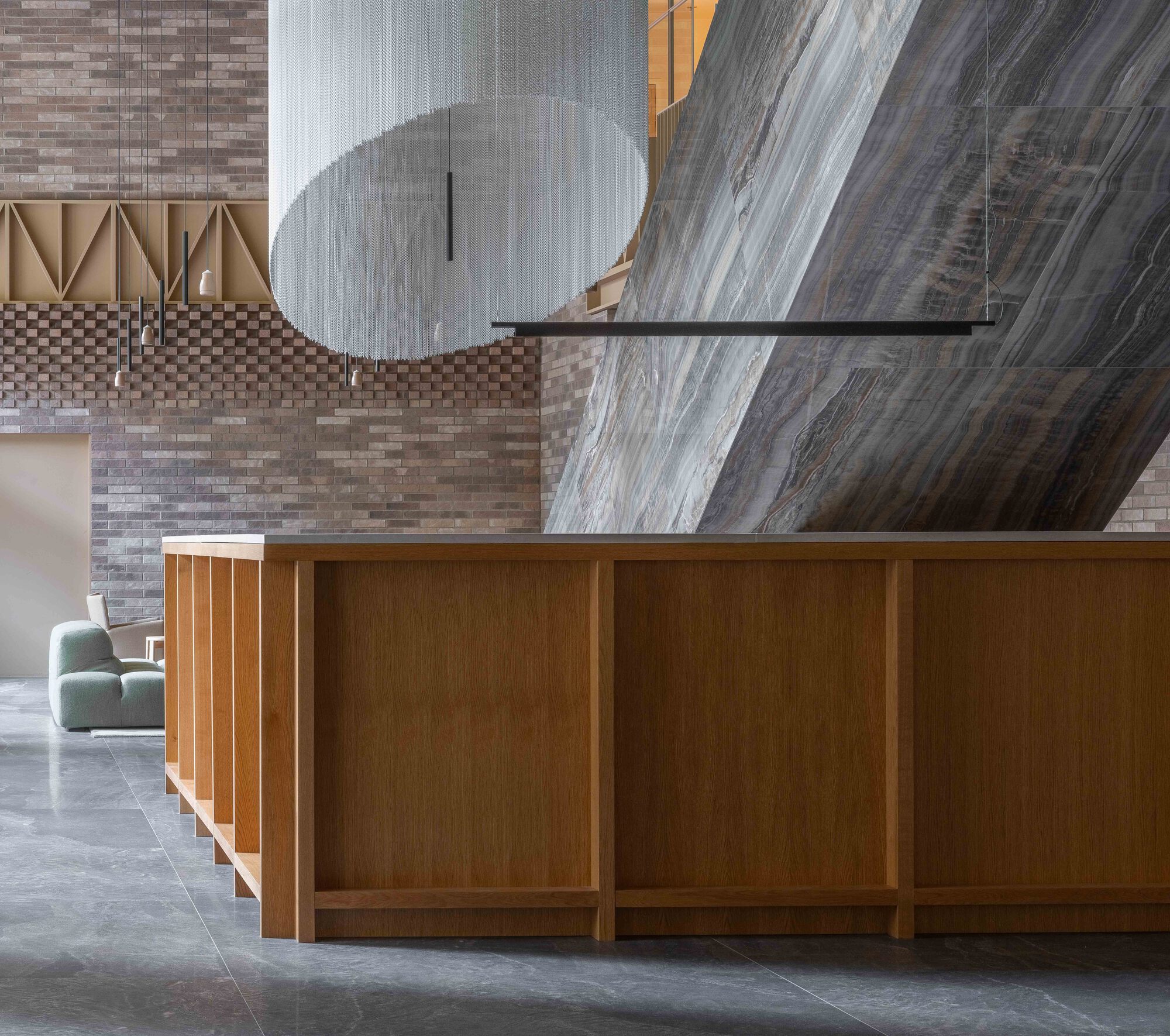 Reception desk with timber paneling below suspended sculptural element and brick wall beyond