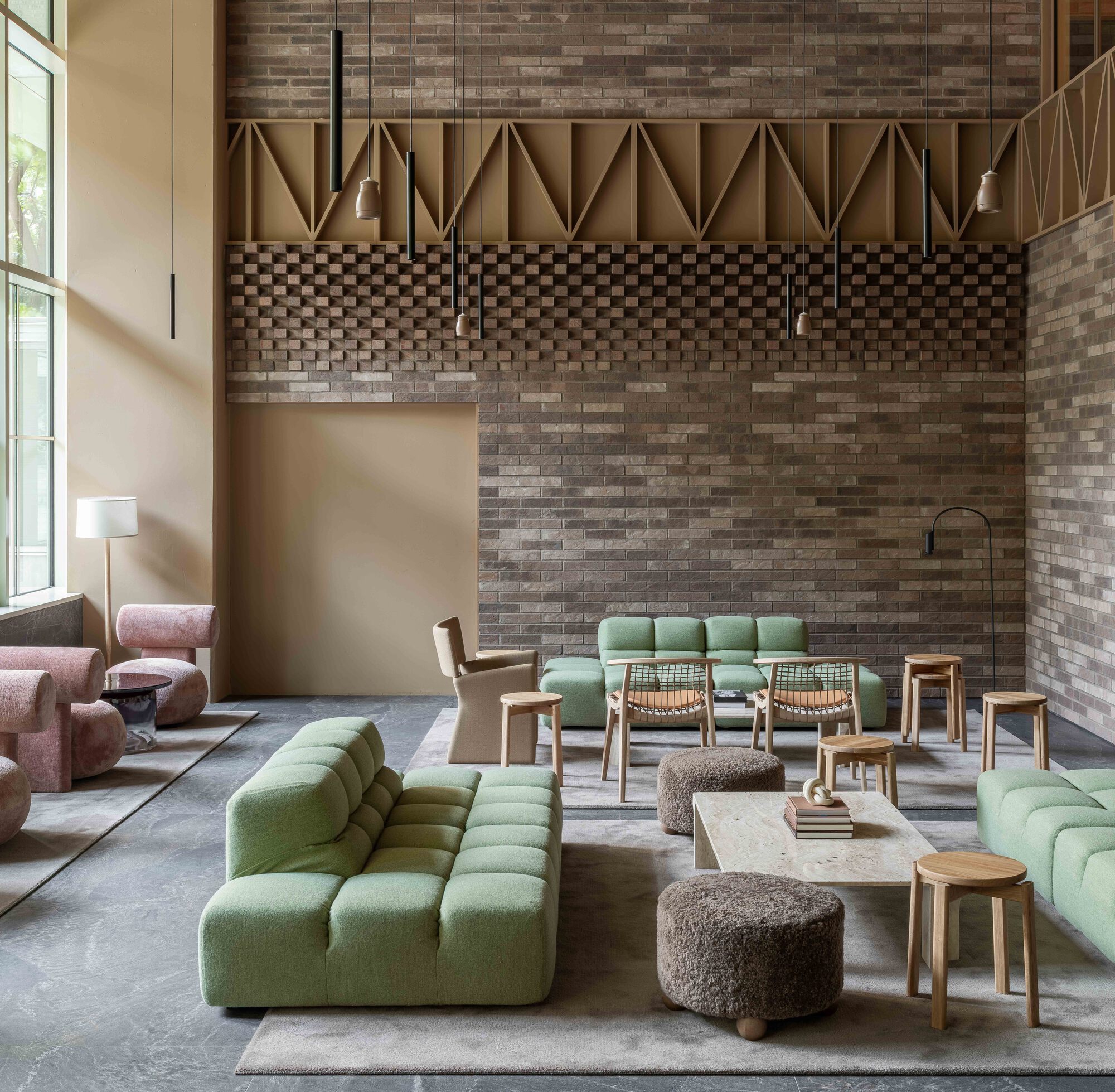 Double-height lounge with variegated brick walls and geometric paneling above green modular seating
