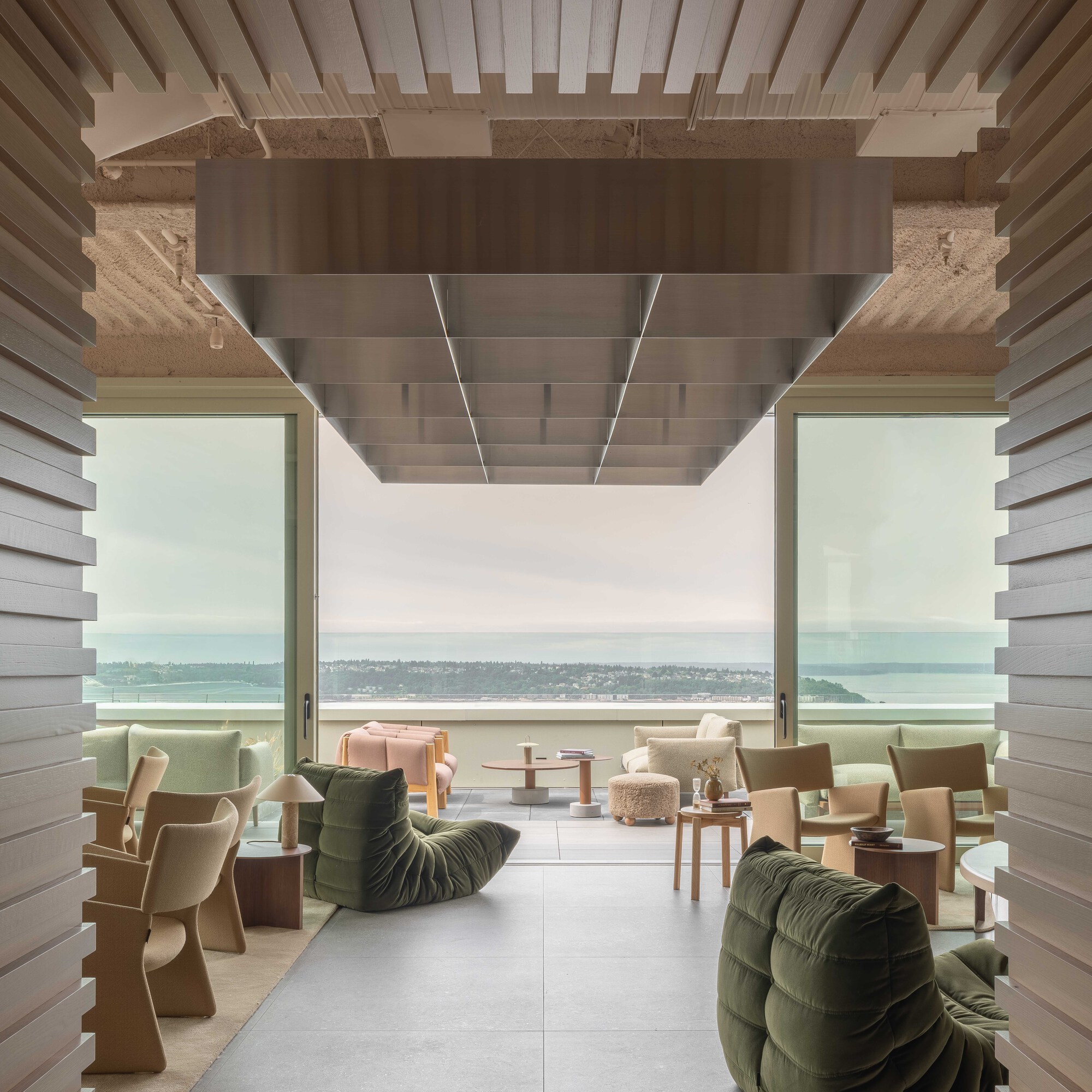 Covered terrace with timber slat ceiling and rammed earth beam framing water views in soft daylight