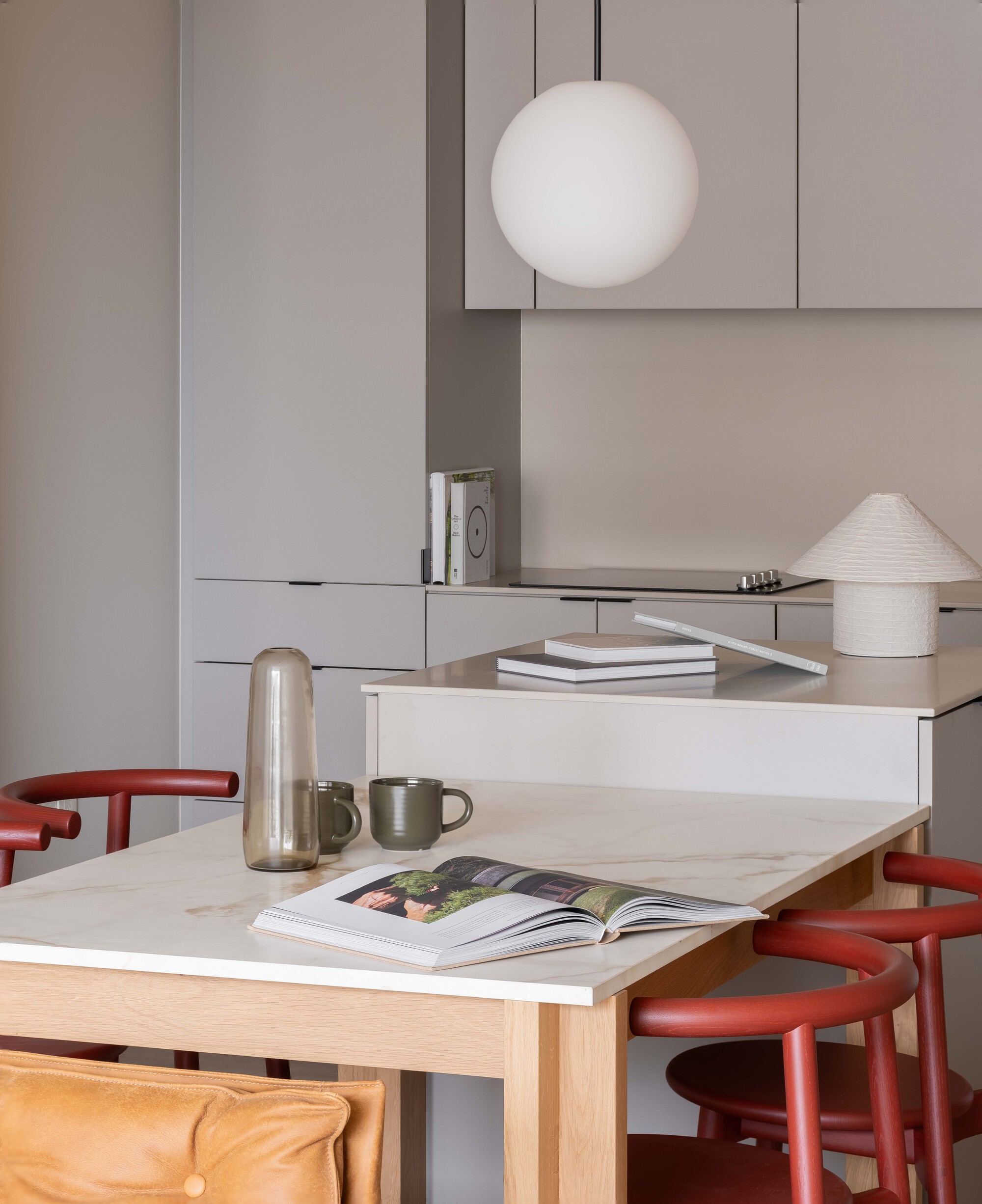 Marble dining table with open magazine, thermal carafe, and red curved stools beneath pendant fixture