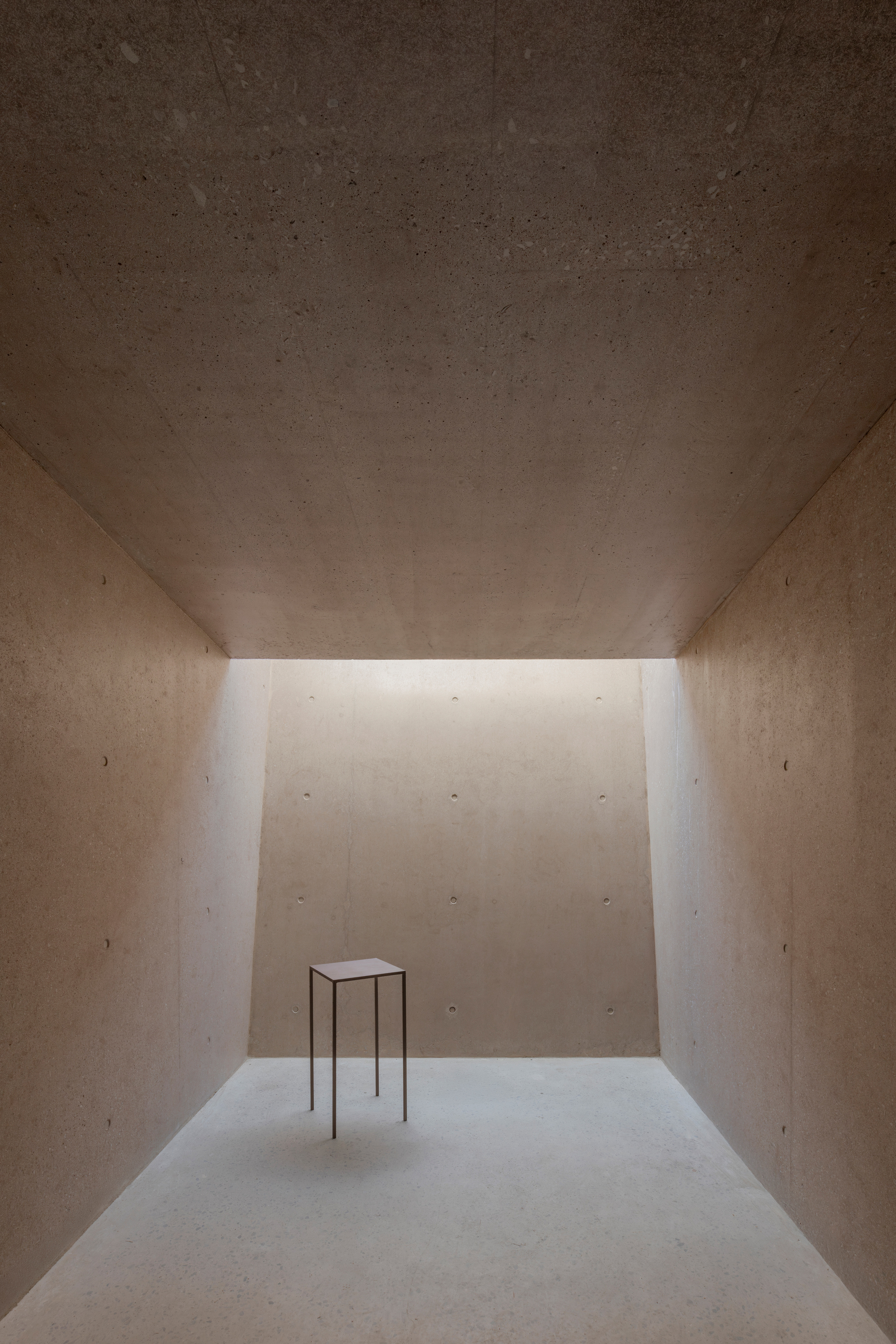 Interior gallery space with clerestory lighting and solitary metal table on pale floor
