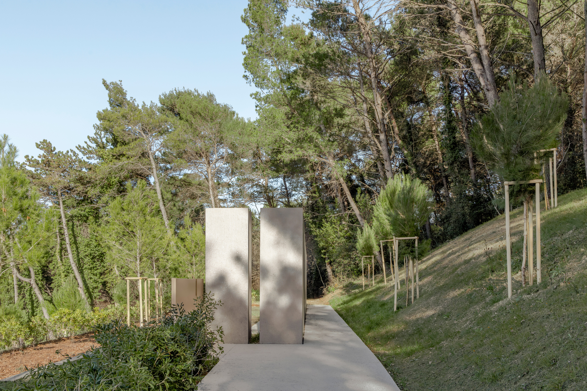 Paired concrete panels forming a gateway along the pathway with newly planted saplings on the slope