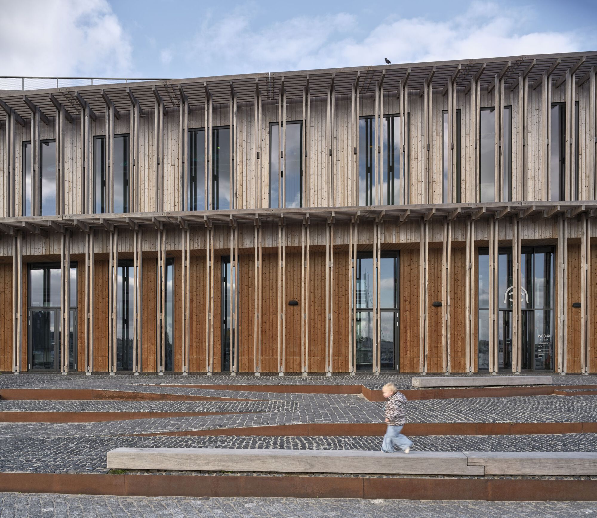 Close-up of the vertical timber screen with inset glazing and a child running along the terrace