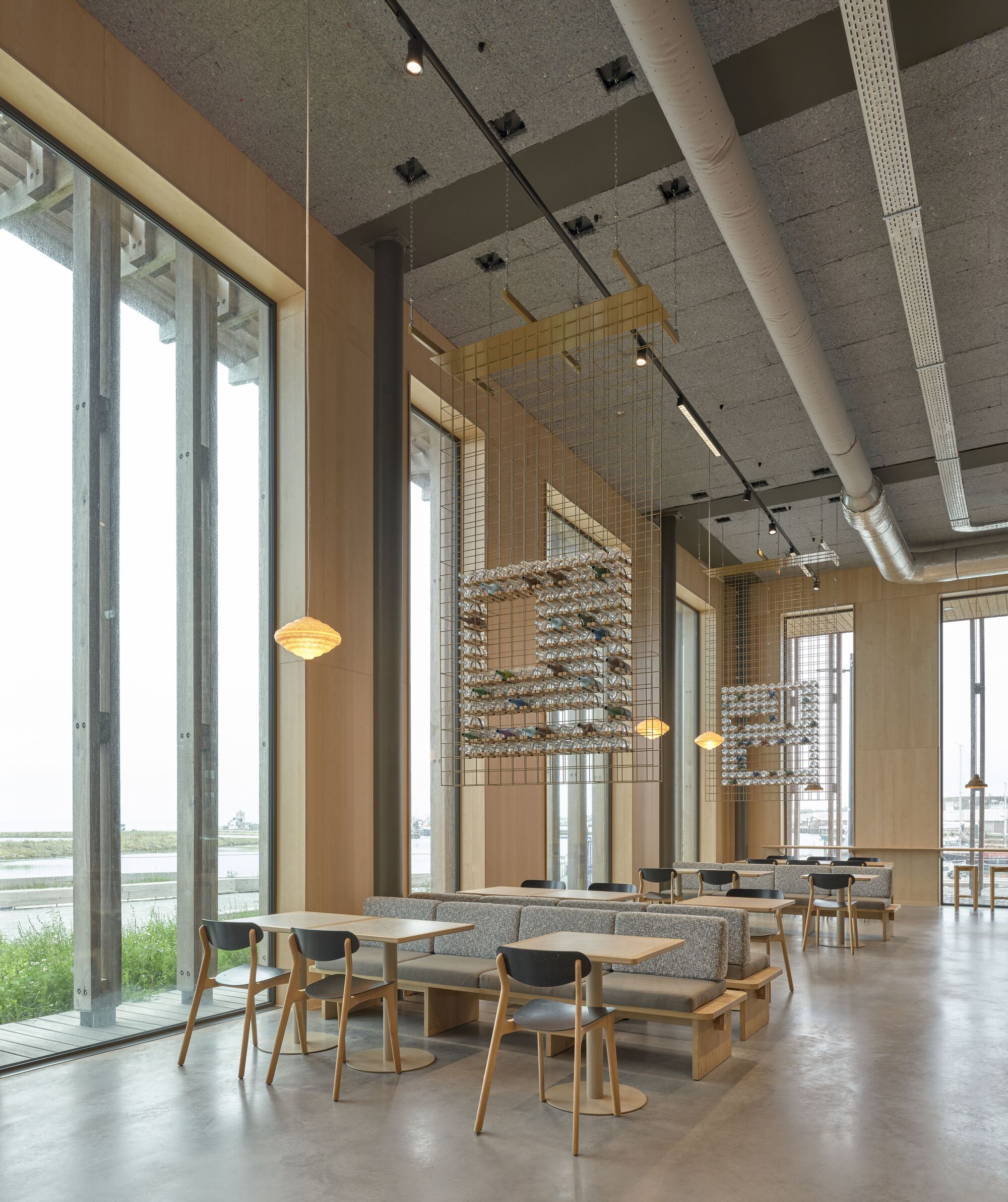 Double-height reading room with timber seating, suspended wire mesh screens and exposed concrete ceiling