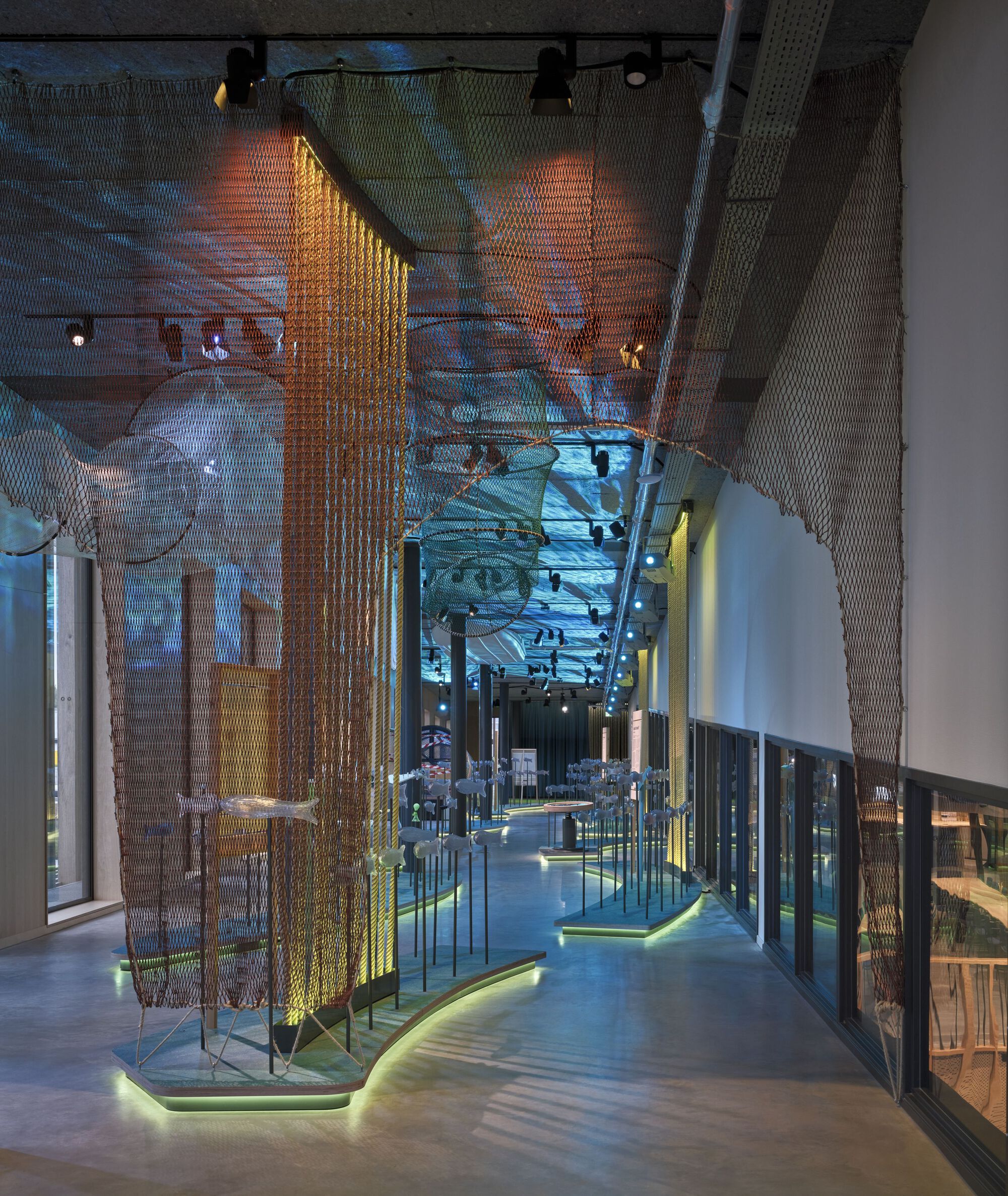 Mirrored ceiling reflecting illuminated brass mesh screens and walkway between glass display cases at twilight