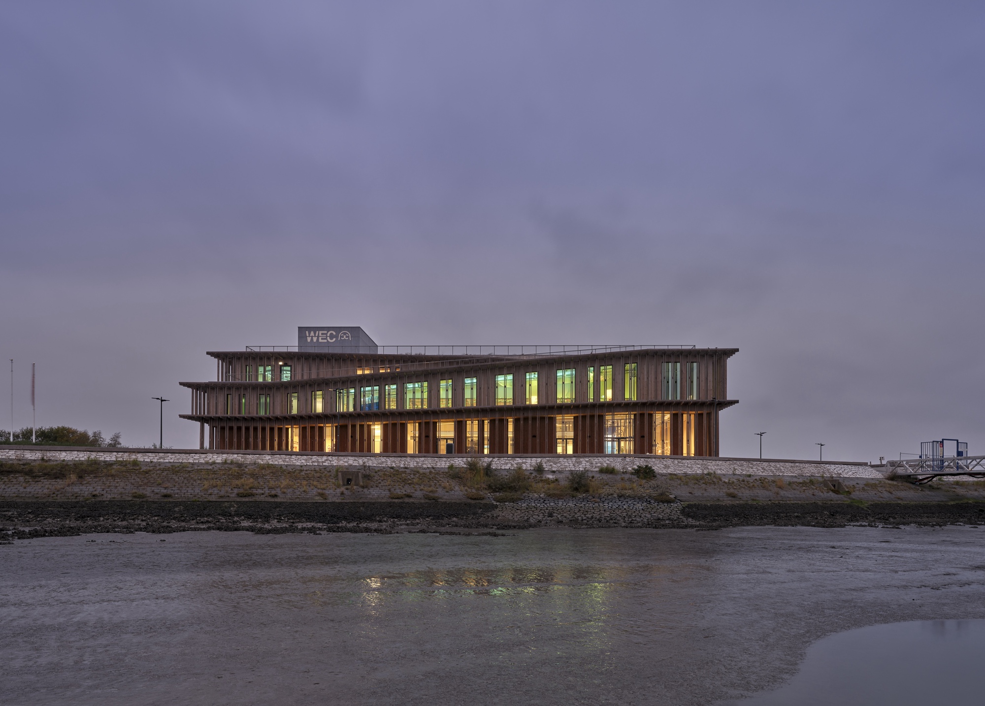 Timber-louvred facade with illuminated interiors viewed from the waterfront at dusk