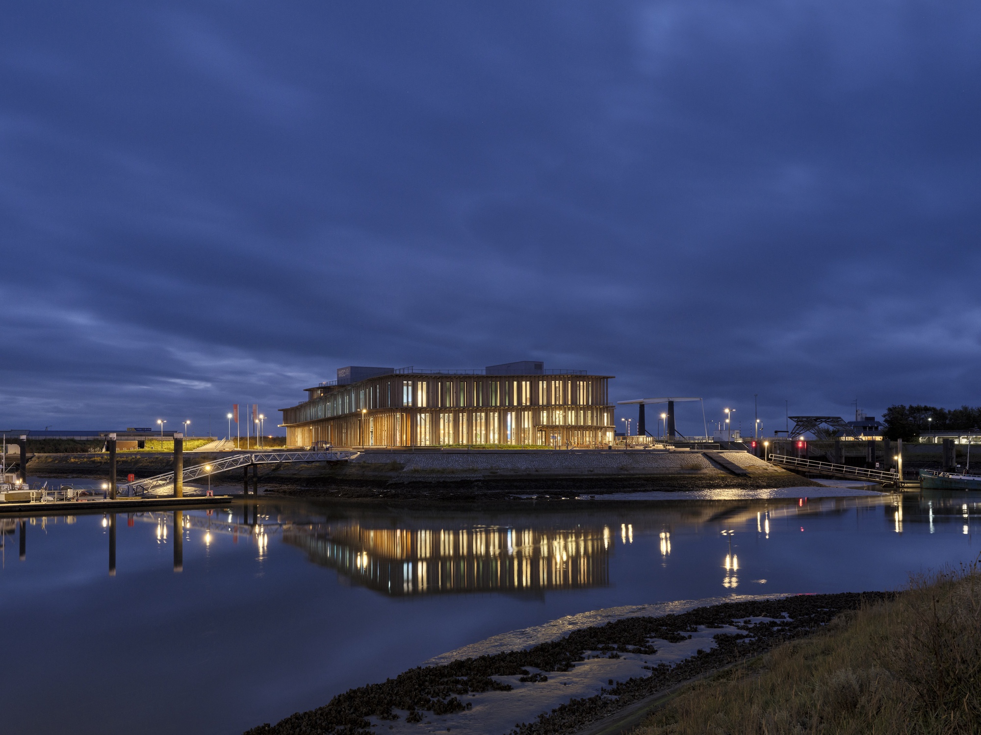 Illuminated building reflecting in calm tidal waters under evening sky with clouds