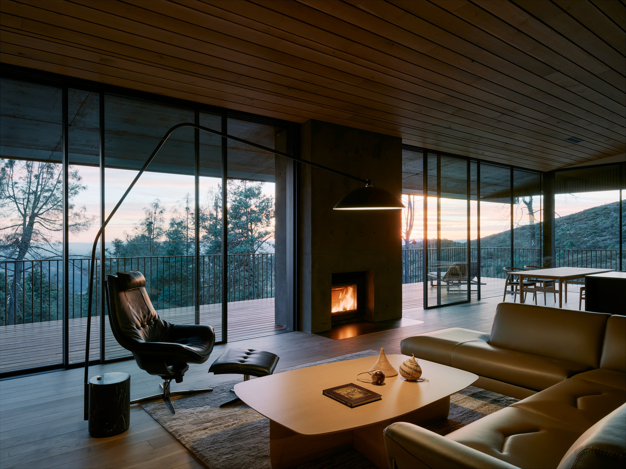 Living room with fireplace and floor-to-ceiling glazing opening to deck at twilight