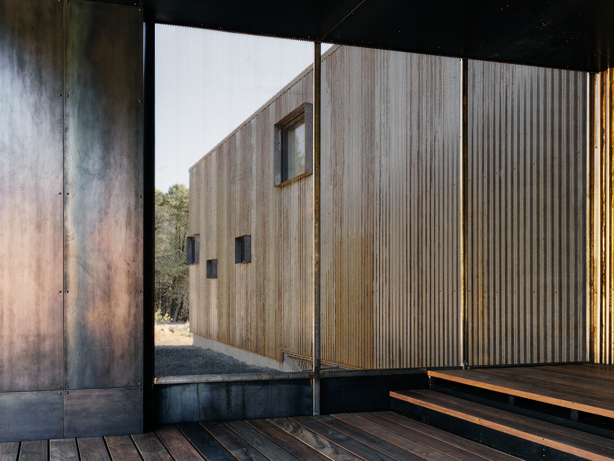 View through sliding glass door to corrugated metal courtyard wall with weathered steel panels flanking the opening