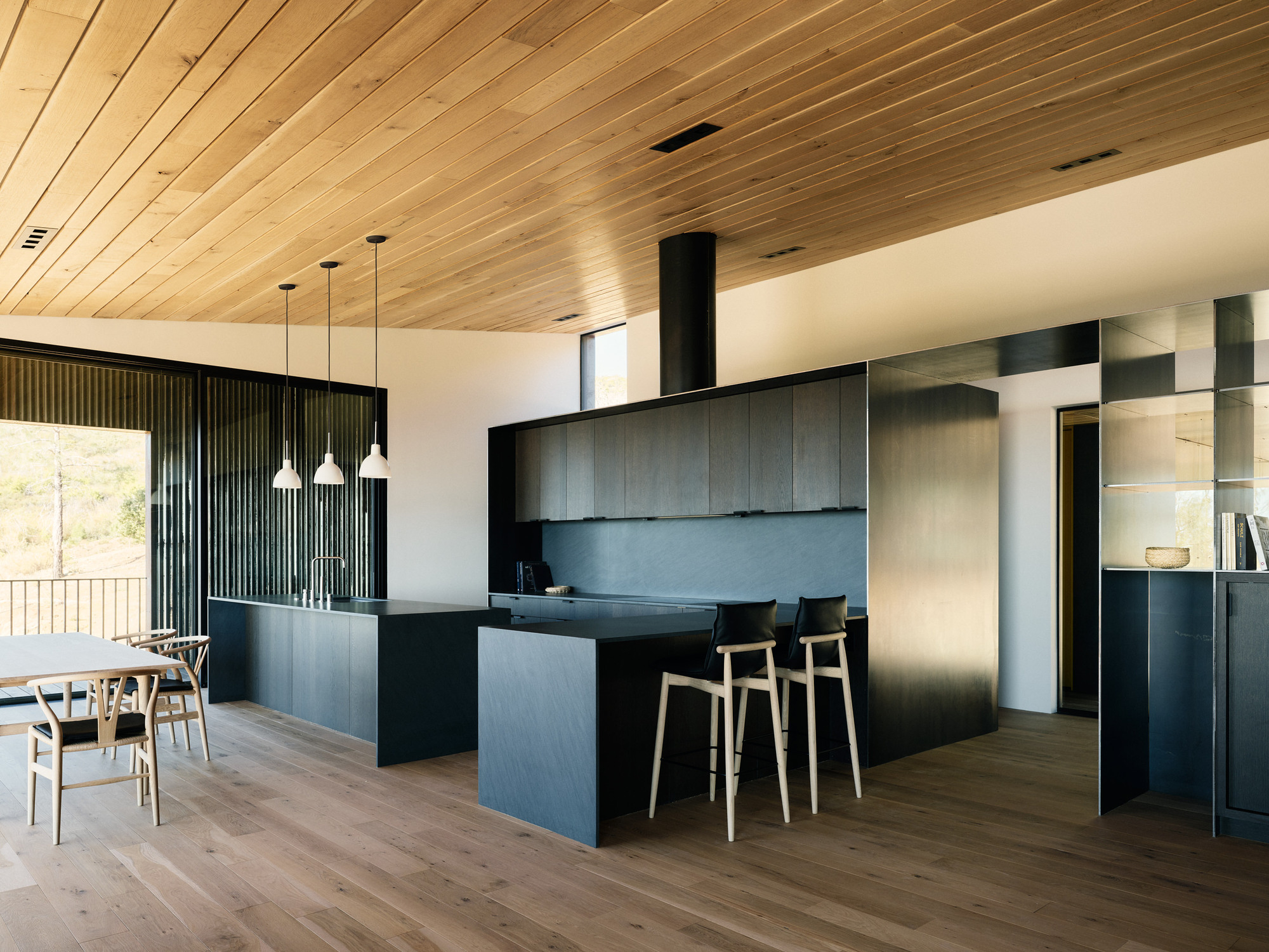Open-plan kitchen and dining area with dark cabinetry, timber-slat ceiling and pendant lights