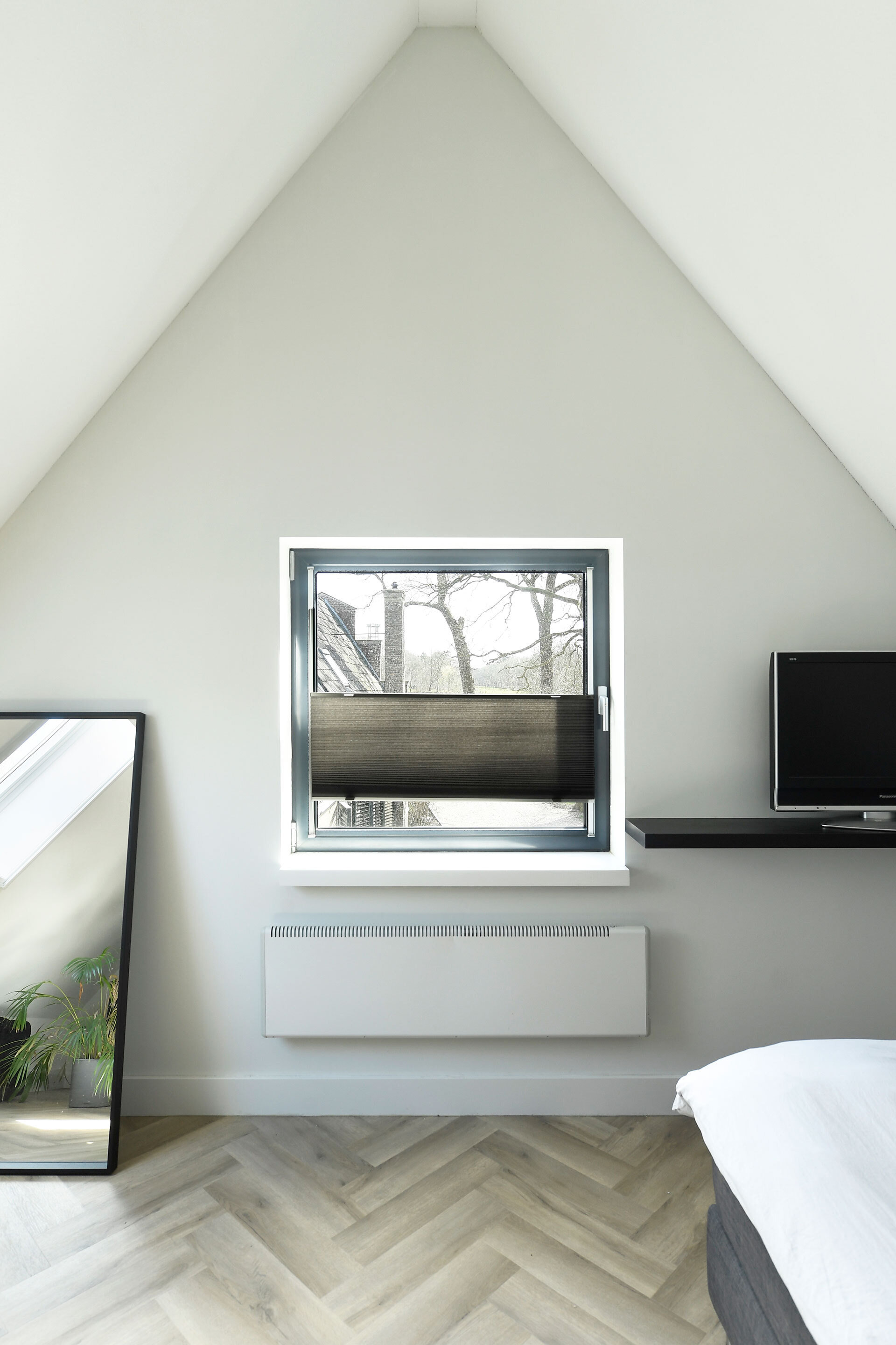 Bedroom window centered in a white gabled wall above a herringbone oak floor