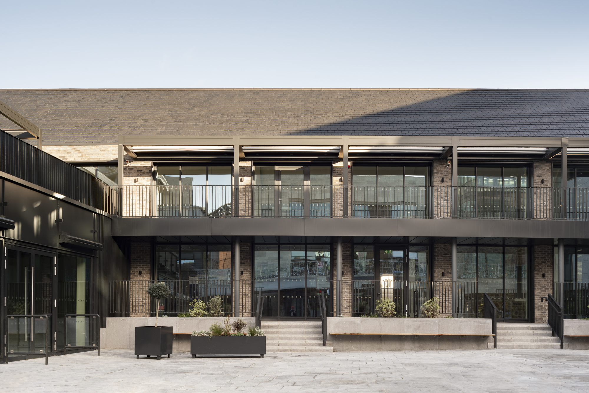 Two-story glazed facade with metal railings and planted boxes opening onto a paved courtyard
