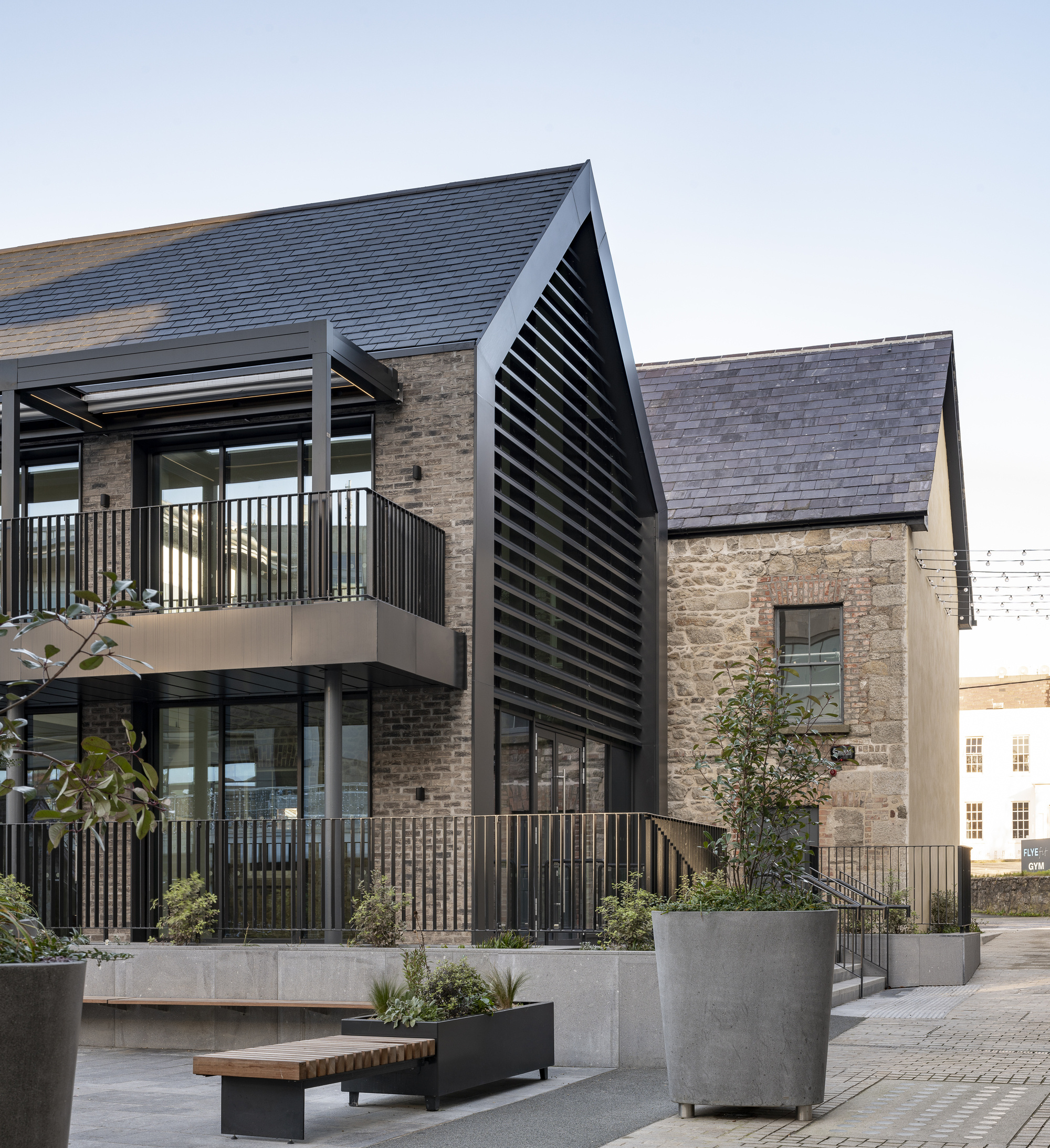Gabled volume with black louvered screen adjacent to stone masonry and planted concrete planters